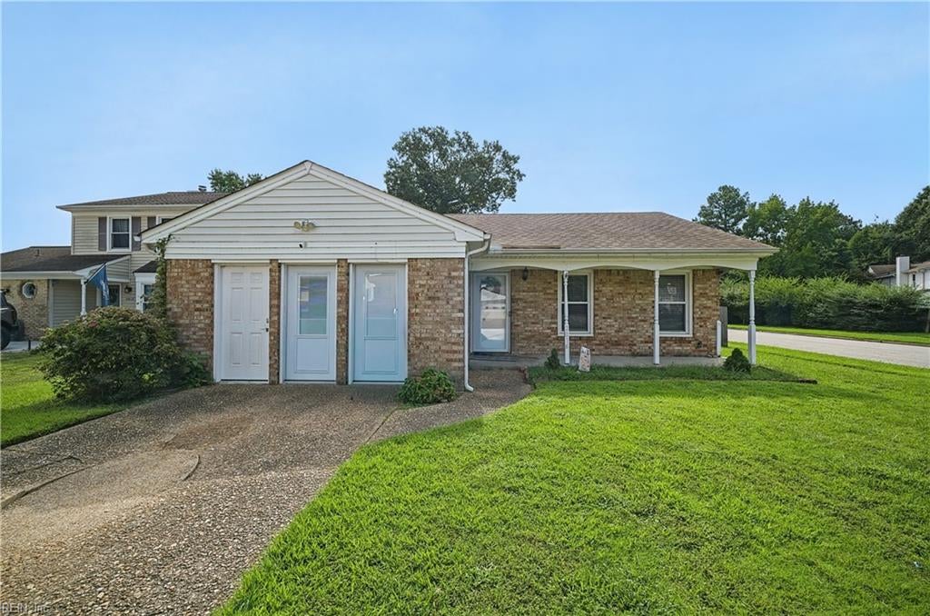 Brick home with a white gabled entry, three front doors, concrete driveway, and green lawn.