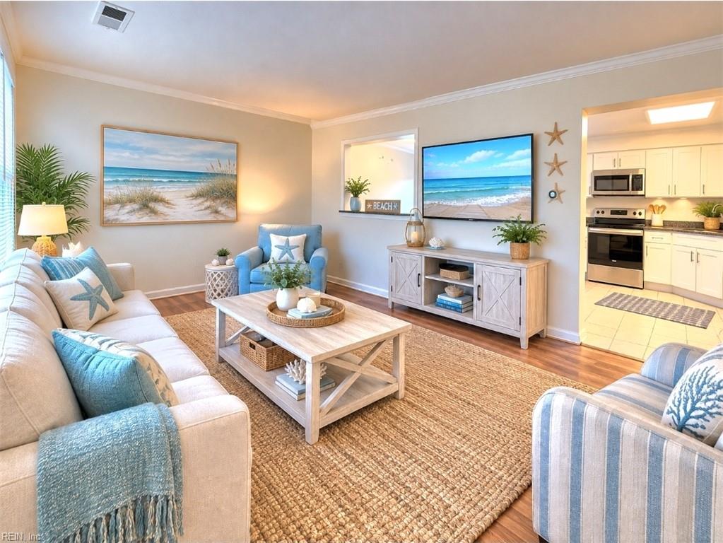 Coastal-styled living room with blue accents, beach artwork, woven rug, and an open kitchen.