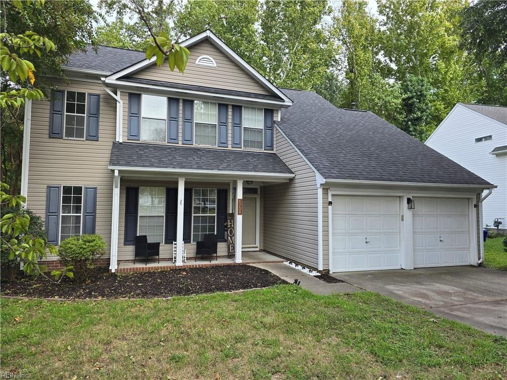 Two-story beige house with blue-gray shutters, a covered porch, and an attached two-car garage.