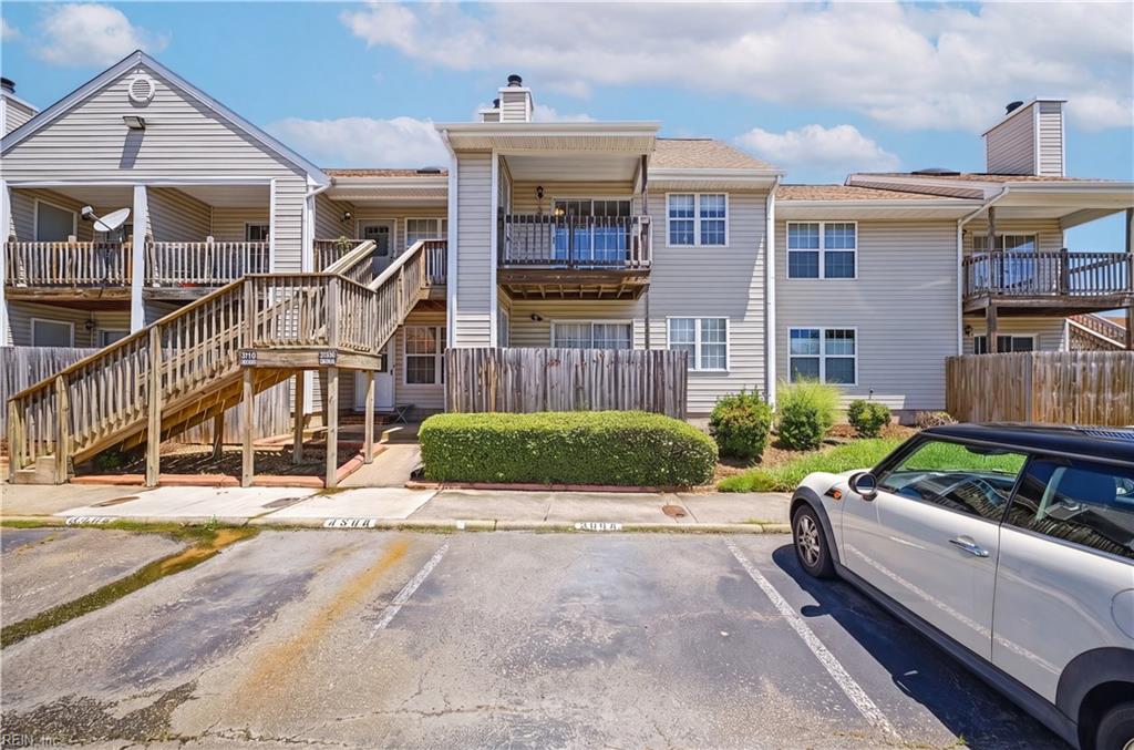 Gray multi-unit building with wooden balconies and exterior stairways beside a parking lot.