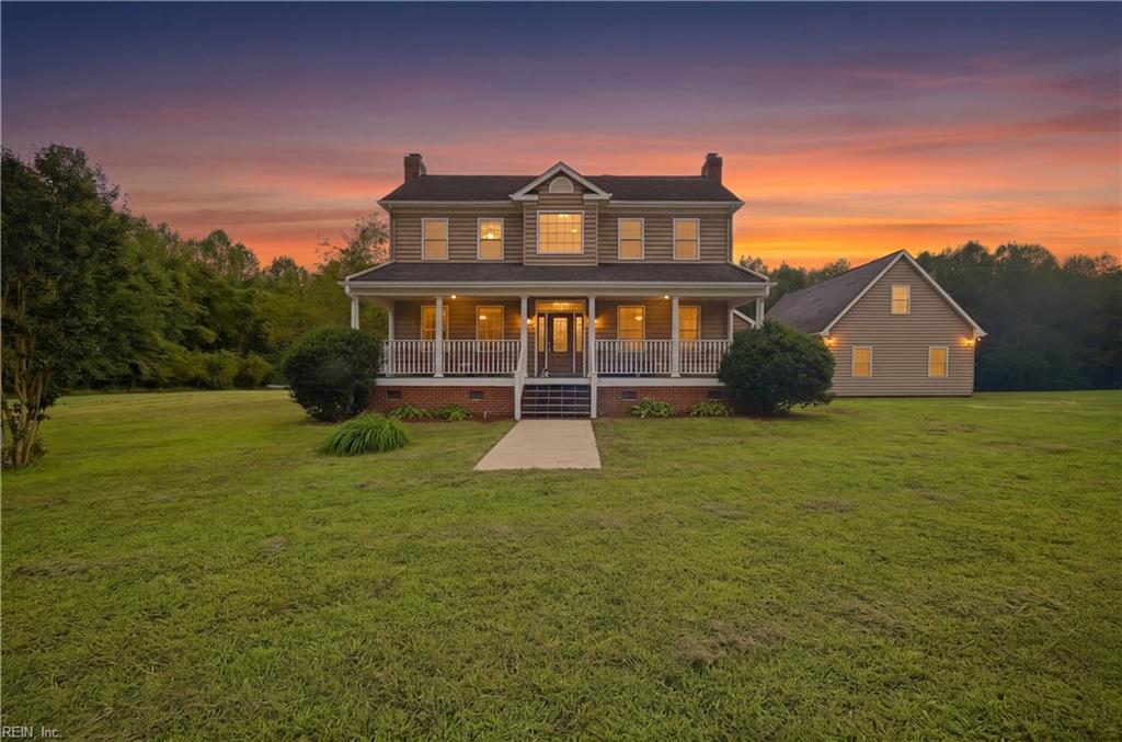 Two-story house with a wide covered porch and broad lawn at sunset.