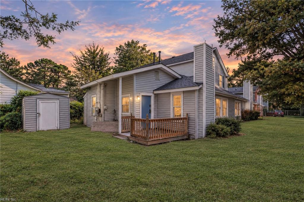 Gray two-story house with a small deck and detached shed at dusk.