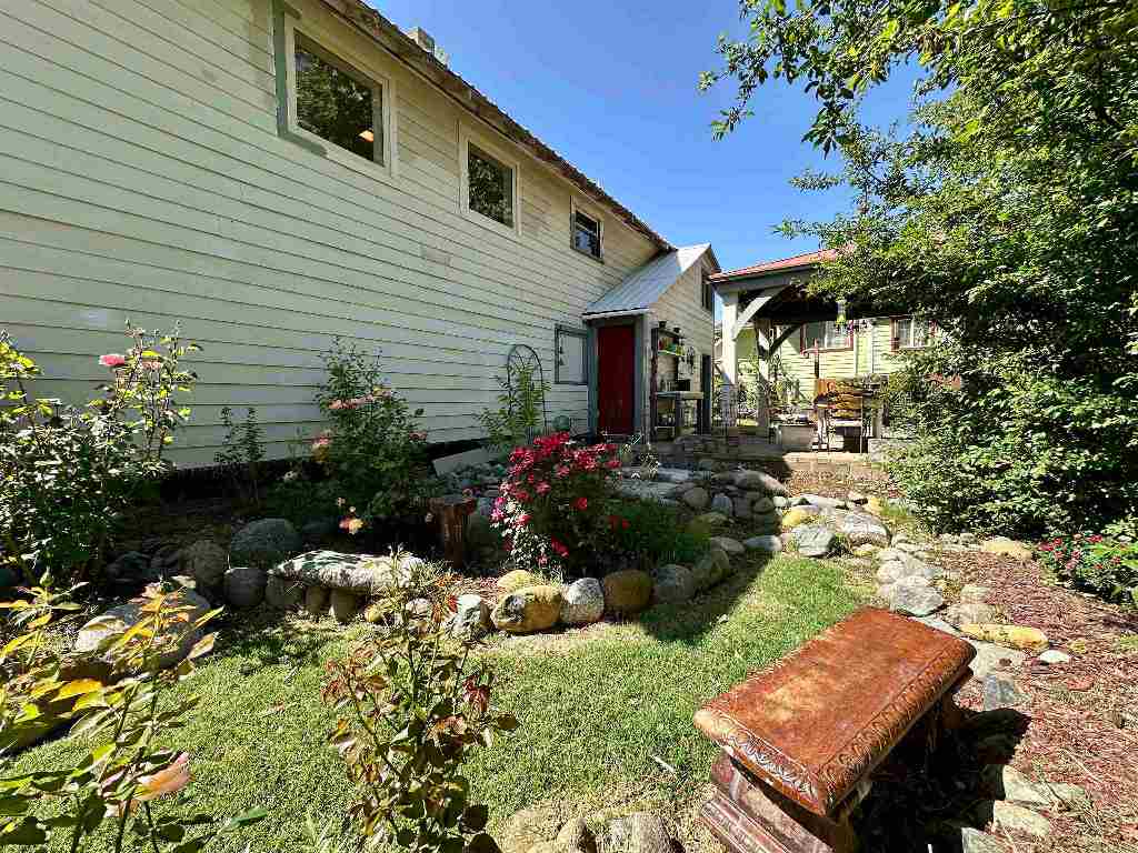Light-sided home with a red door, covered patio, and flowering rock garden.