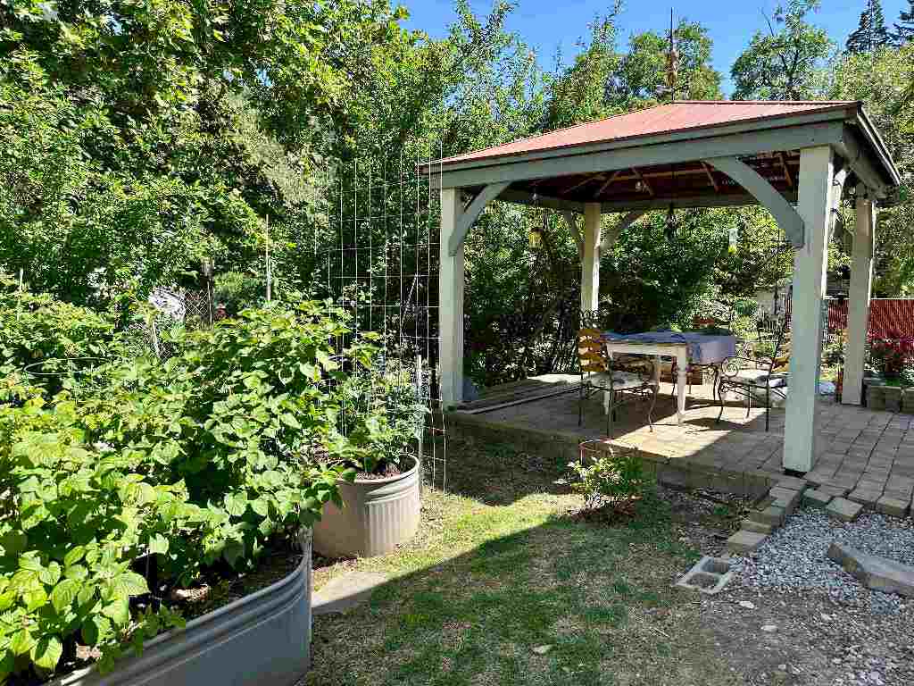 Covered patio with outdoor dining furniture beside leafy raised garden planters.