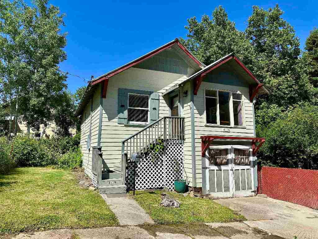 House with pale siding, red roof trim, a raised lattice-front porch, and two lower garage doors.