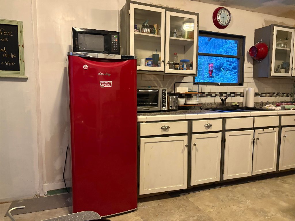 Kitchen with a red refrigerator, cream cabinets, and a window overlooking trees.