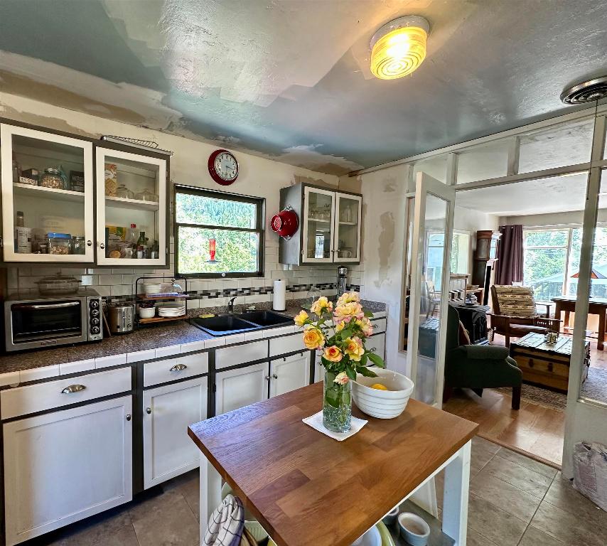 Kitchen with white cabinets, dark counters, a central butcher-block table, and adjoining sunlit living room.