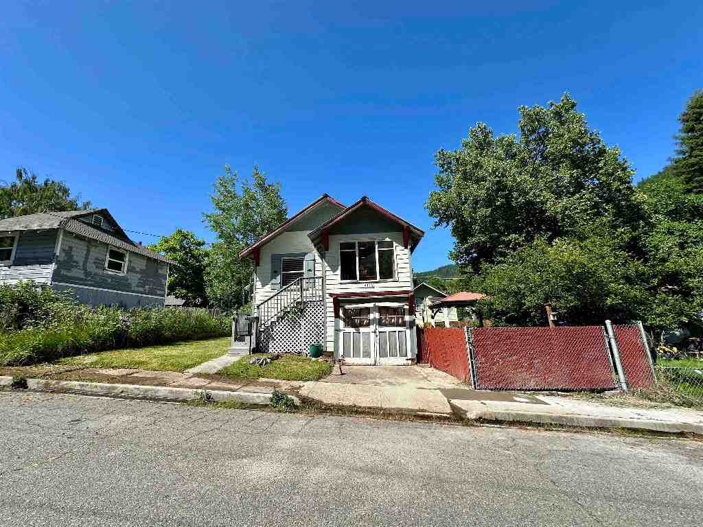 Two-story house with red roof trim, front steps, and a red chain-link fence along the sidewalk.