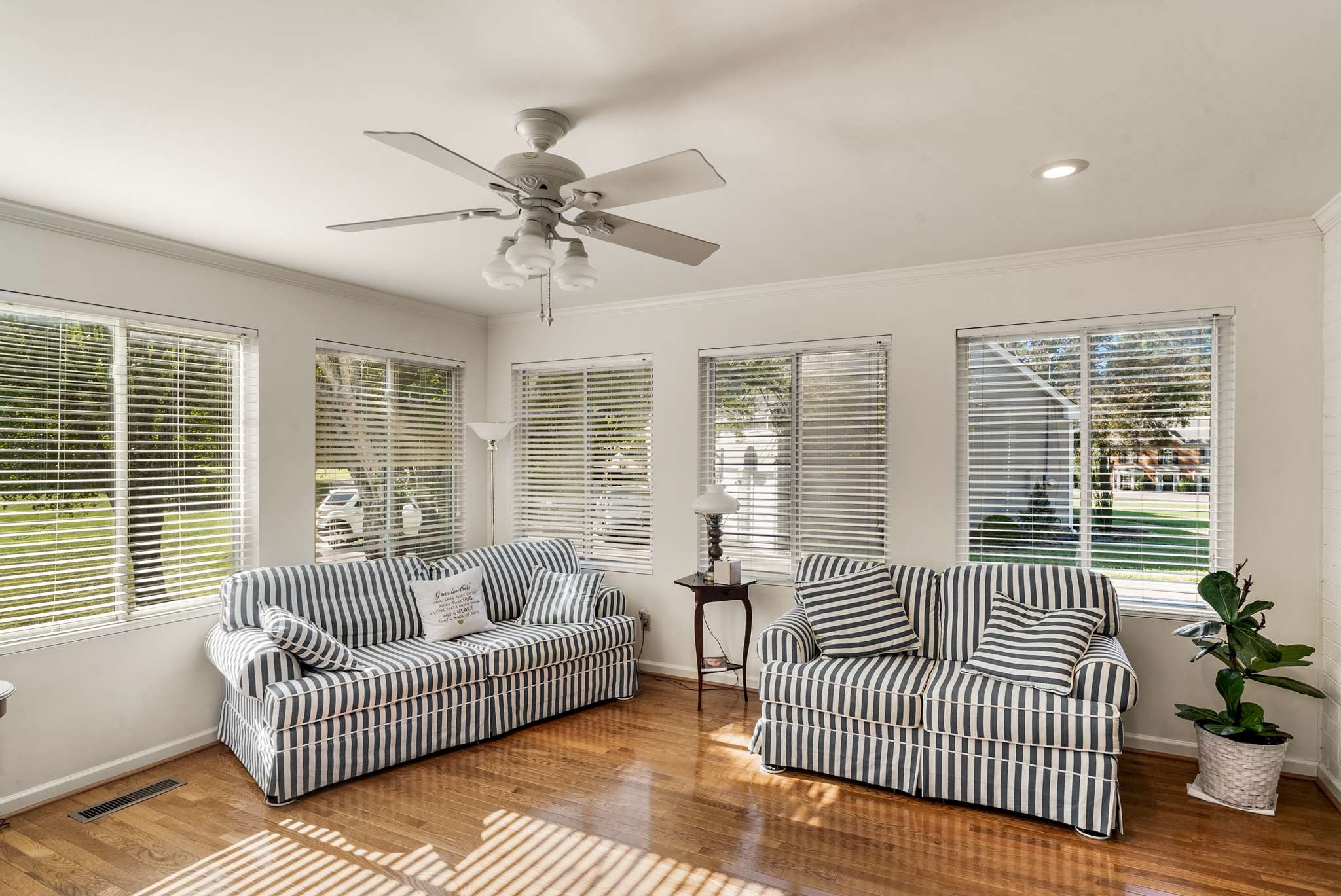 Living room with striped sofas, hardwood floors, and sunlight through several windows.