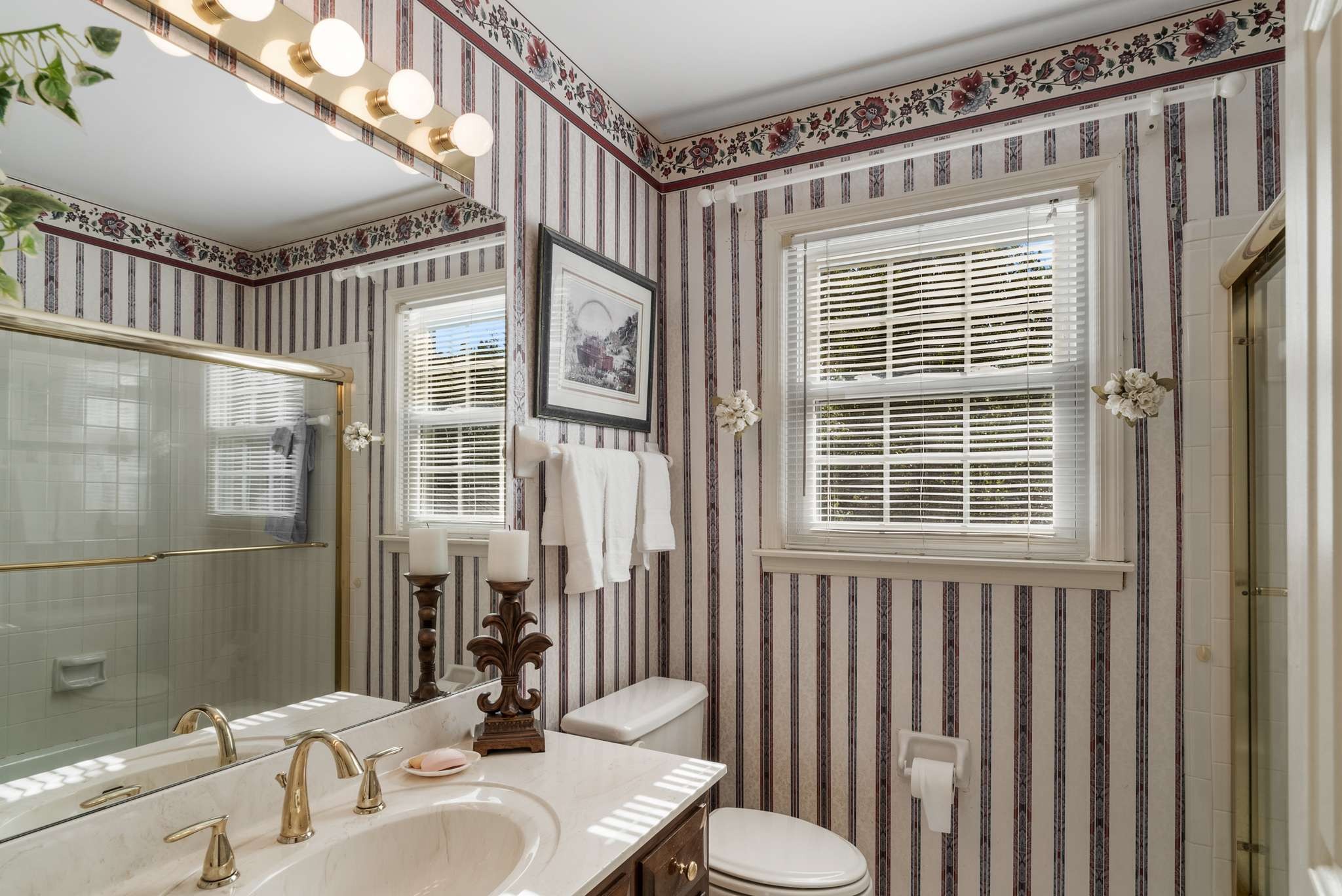 Bathroom with floral striped wallpaper, a marble vanity, and a glass-enclosed shower.