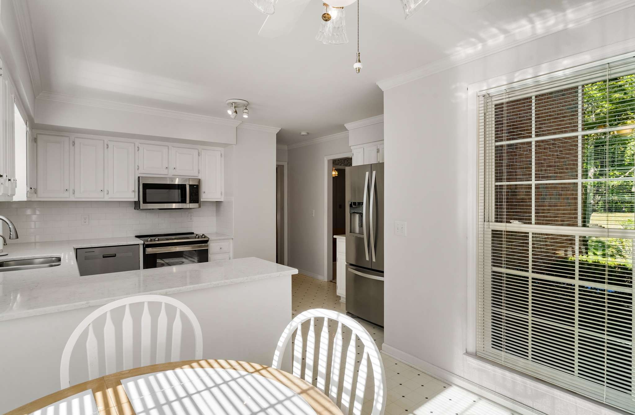 Bright white kitchen with stainless steel appliances, a peninsula, and a sunlit dining table by the window.