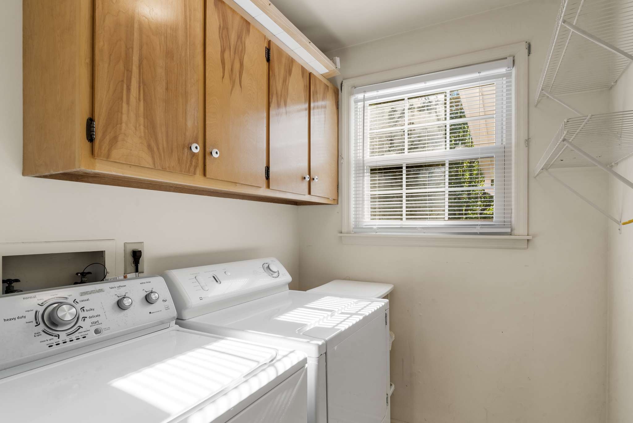Laundry room with washer and dryer, wood cabinets, and a sunlit window.
