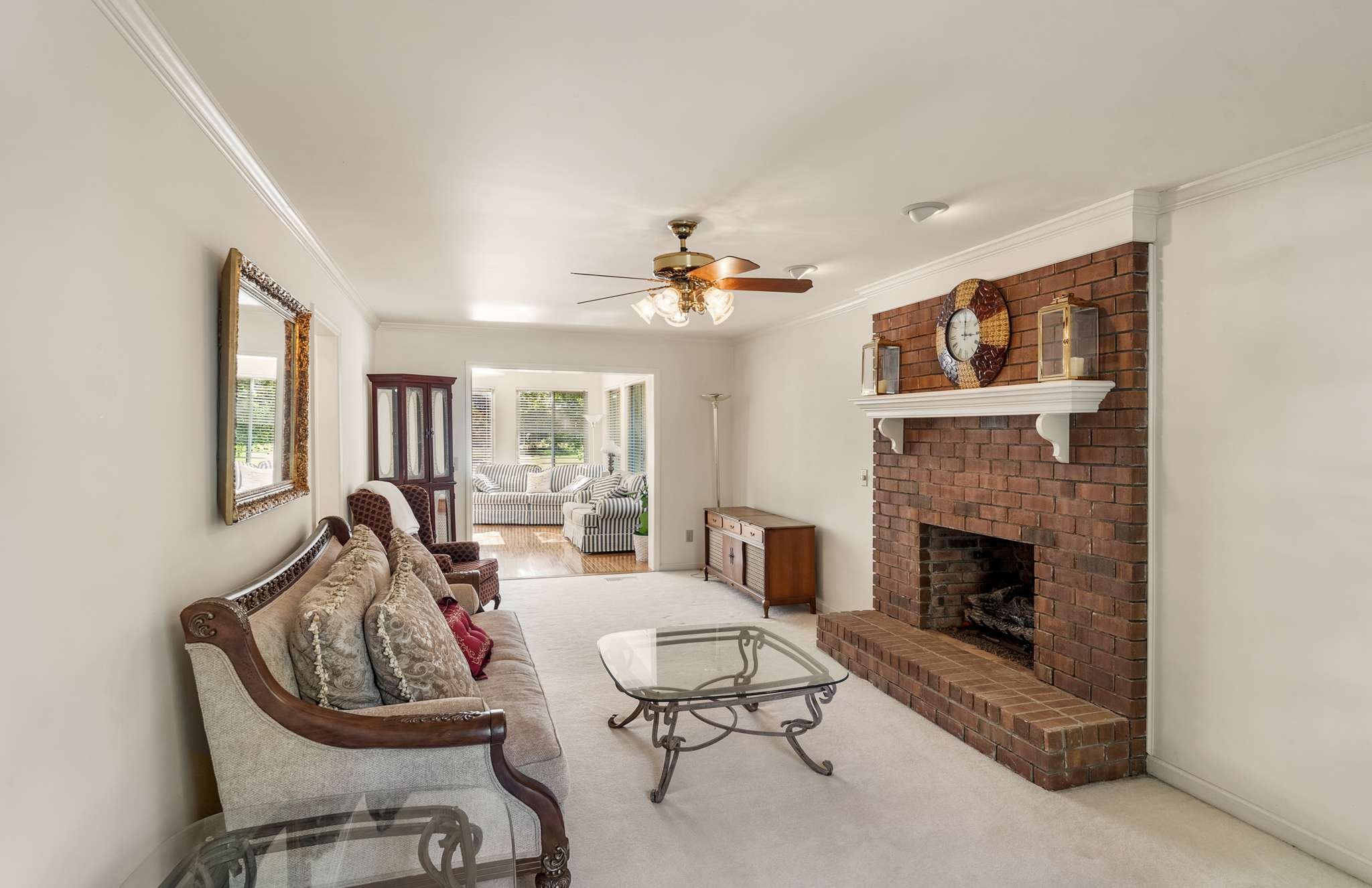 Furnished living room with a large brick fireplace and a wide opening to a bright adjoining sitting room.