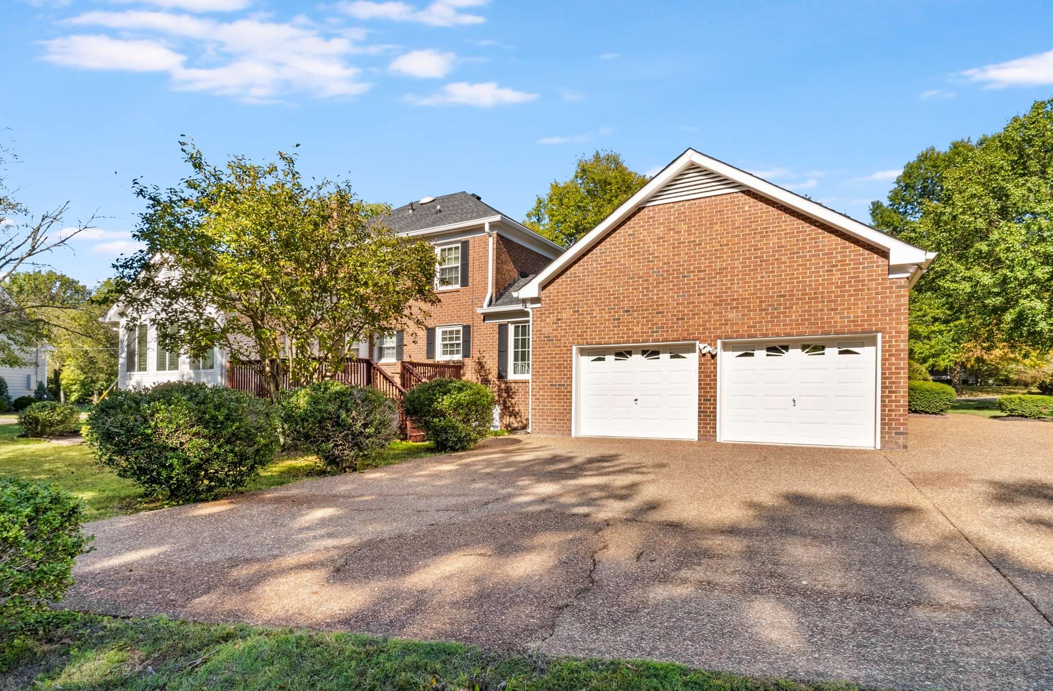 Two-story brick house with two garage doors and a wide driveway, framed by mature trees.