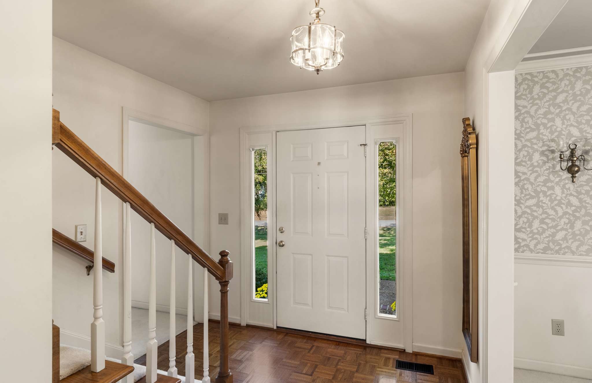 Entry foyer with a white front door, parquet flooring, and a staircase with a wood handrail.