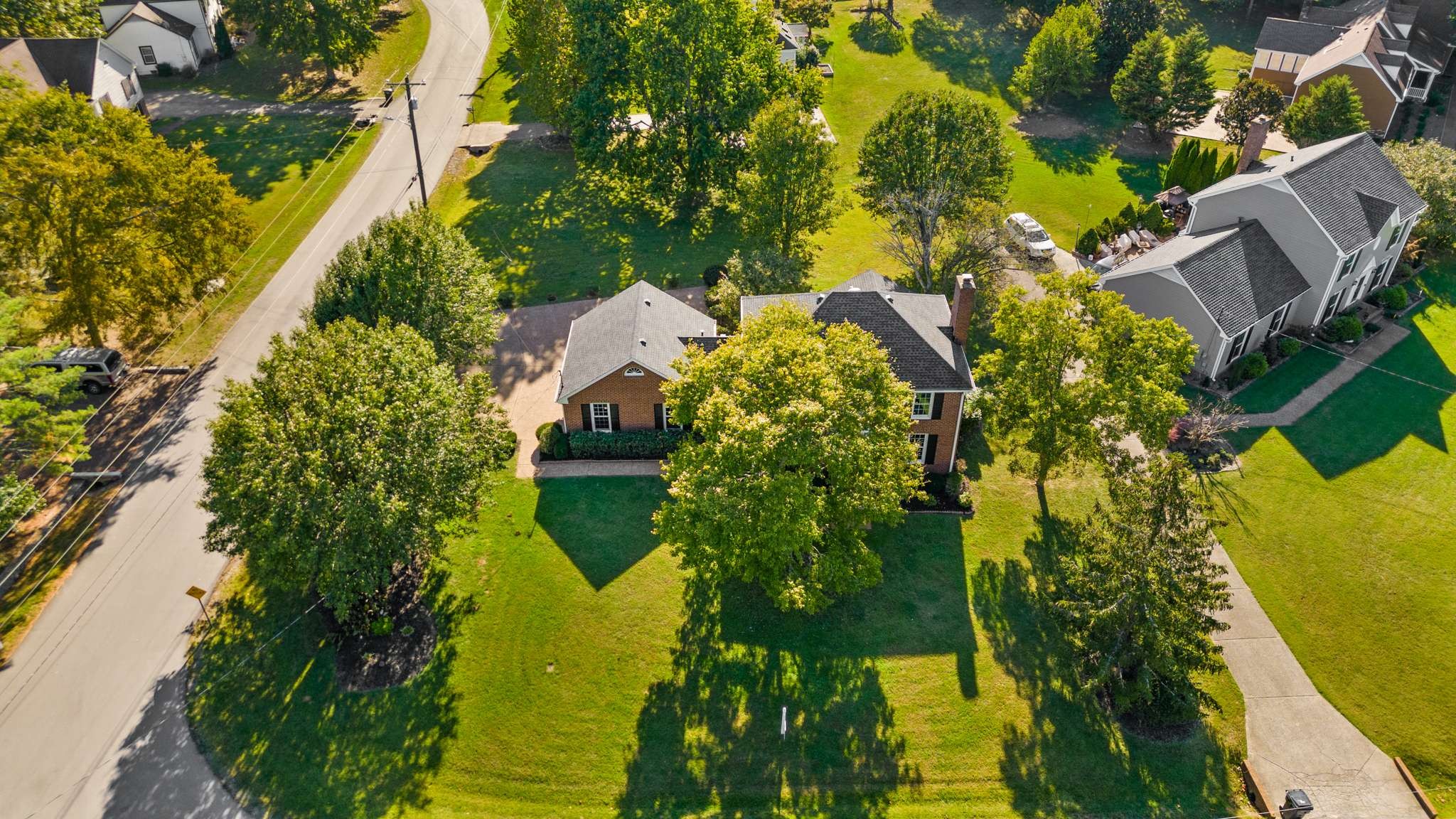 Aerial view of a brick home surrounded by mature trees and a broad lawn.