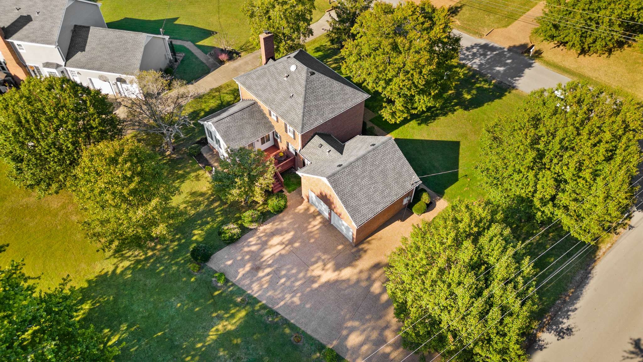 Two-story brick home with a broad driveway and mature trees, seen from above.