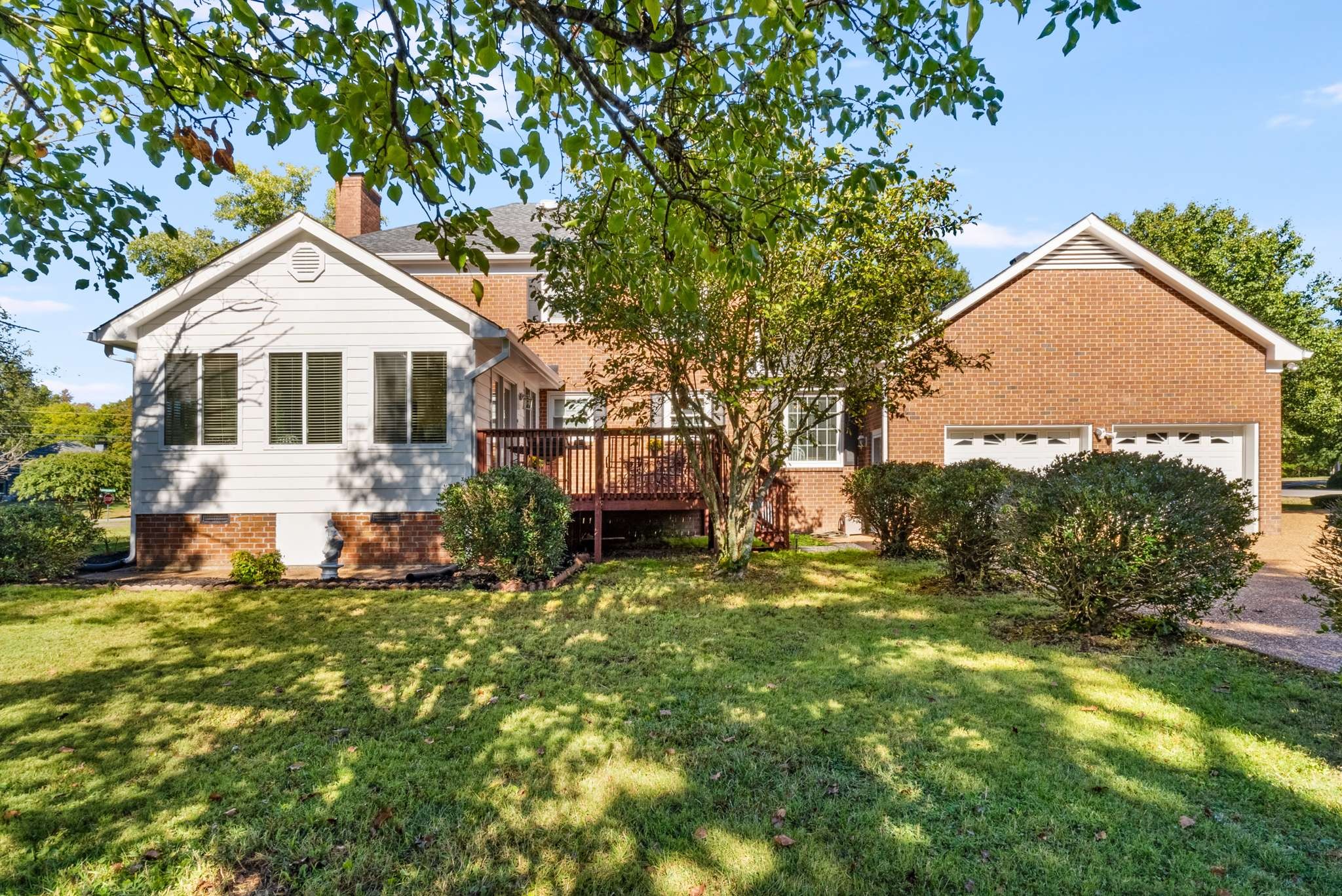Brick home with a two-car garage and raised deck behind a leafy, shaded lawn.