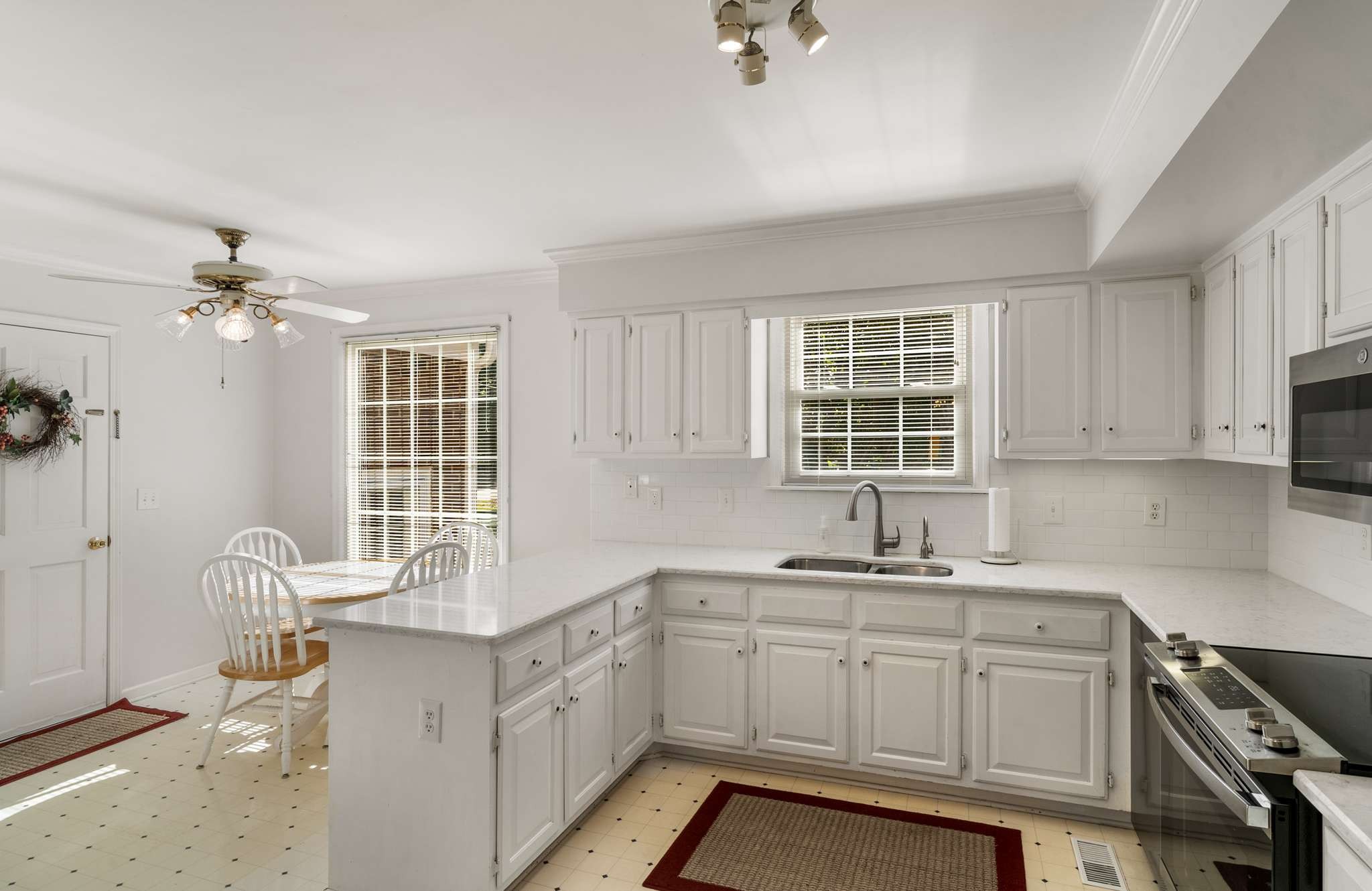 White kitchen with a large peninsula, paneled cabinets, and a dining nook beside the window.
