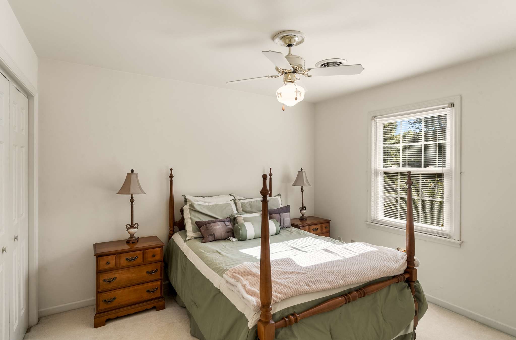 Bedroom with a wooden four-poster bed, sage green bedding, matching dressers, and a sunlit window.
