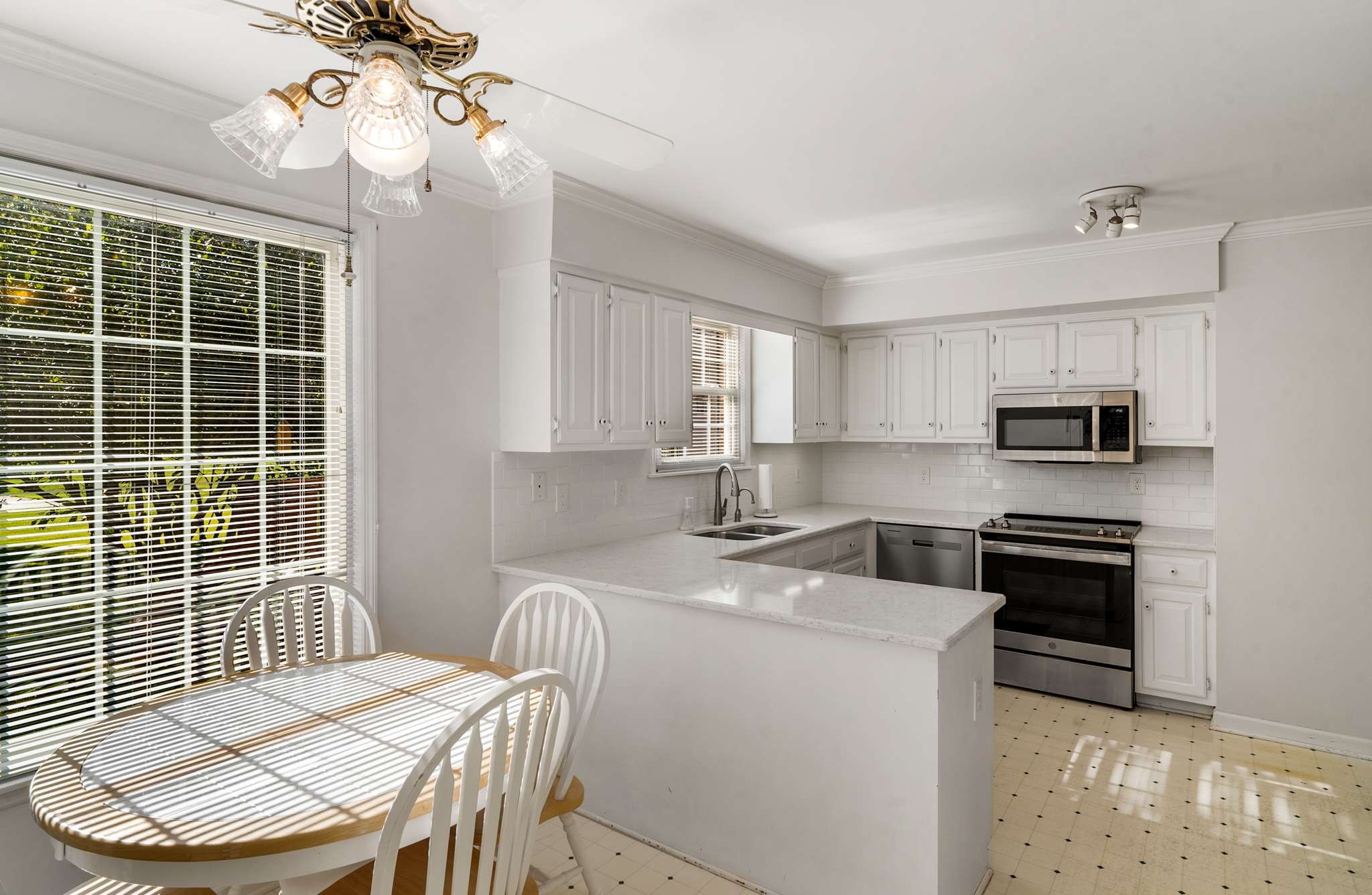 Bright white kitchen with a peninsula and stainless steel appliances beside a sunny dining nook.