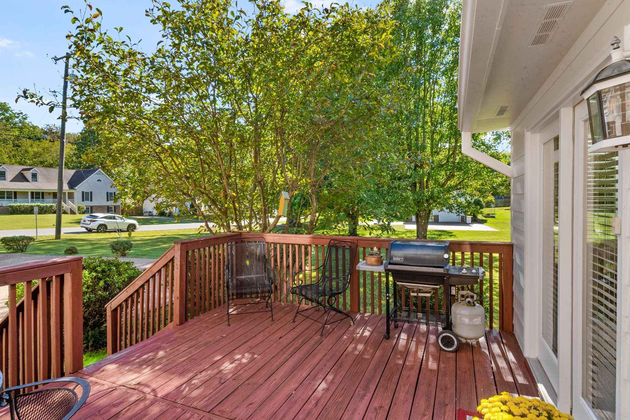 Wooden deck with metal chairs and a gas grill, shaded by mature trees.