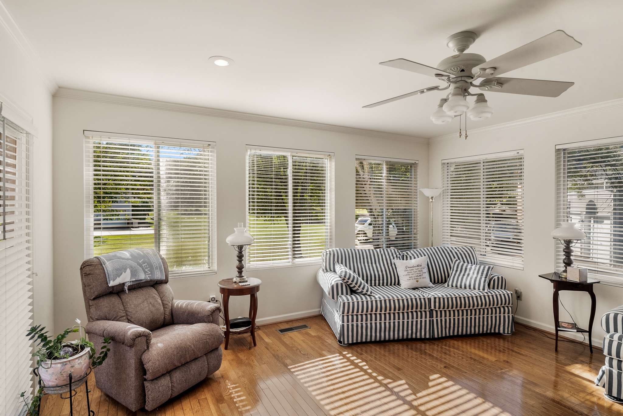 Living room with striped sofa, brown recliner, hardwood floors, and windows with blinds.