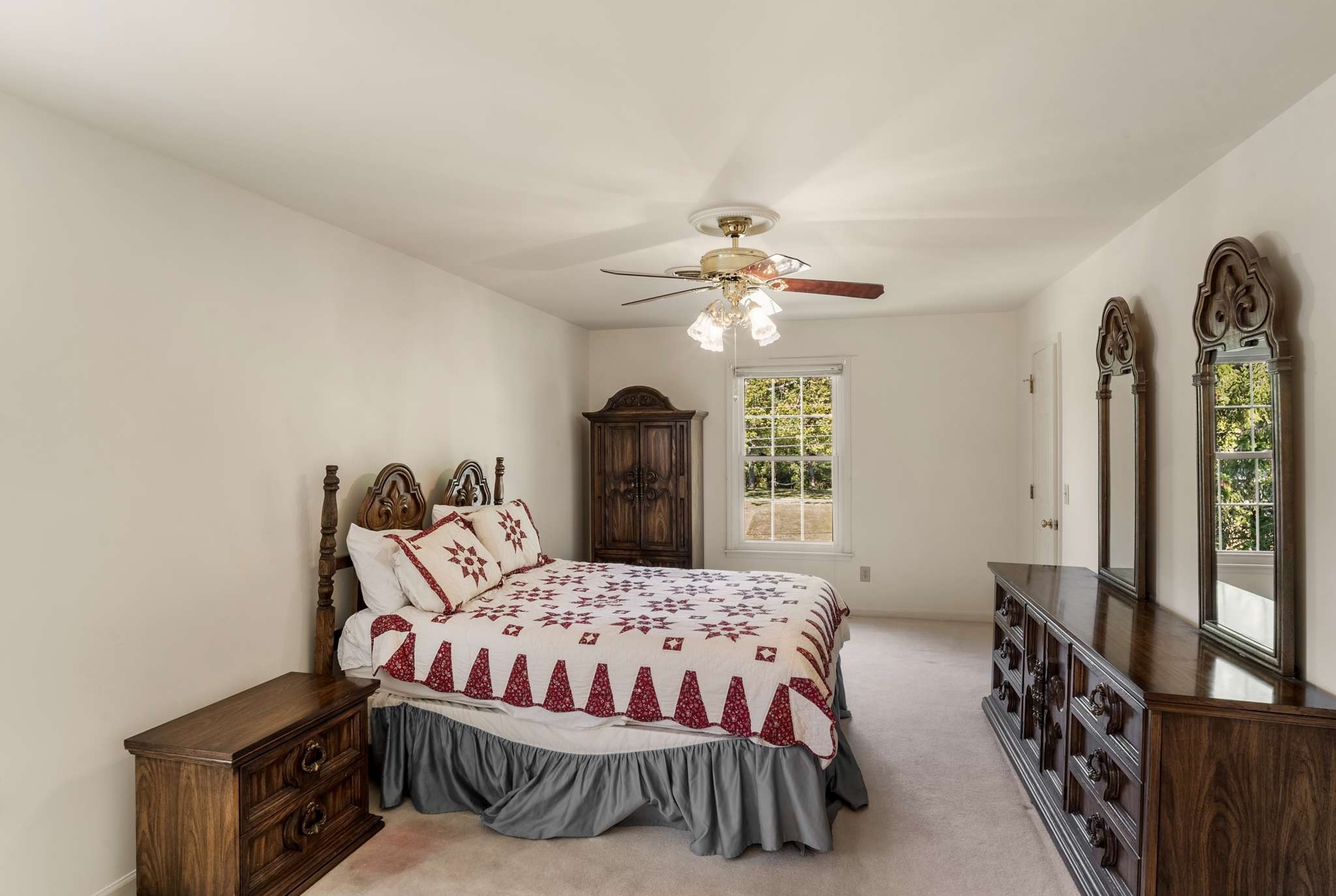 Furnished bedroom with a red-and-white patchwork quilt and carved dark-wood furniture.