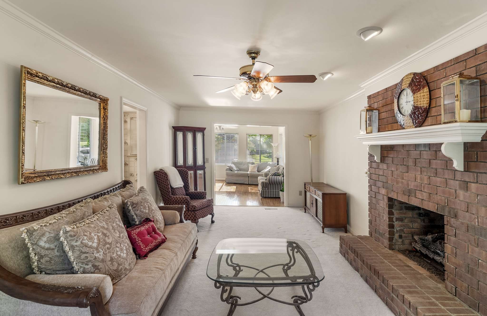 Living room with a brick fireplace, patterned sofas, and a glass coffee table.