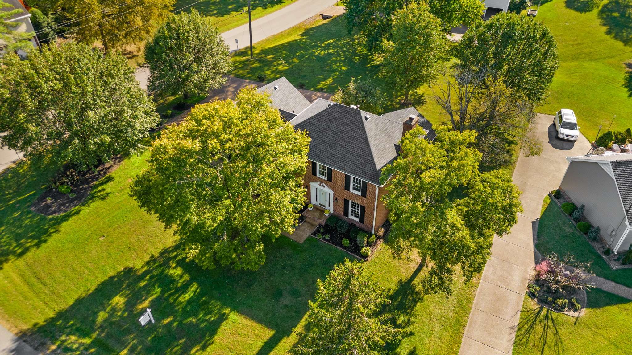 Aerial view of a brick house surrounded by mature trees and a broad green lawn.