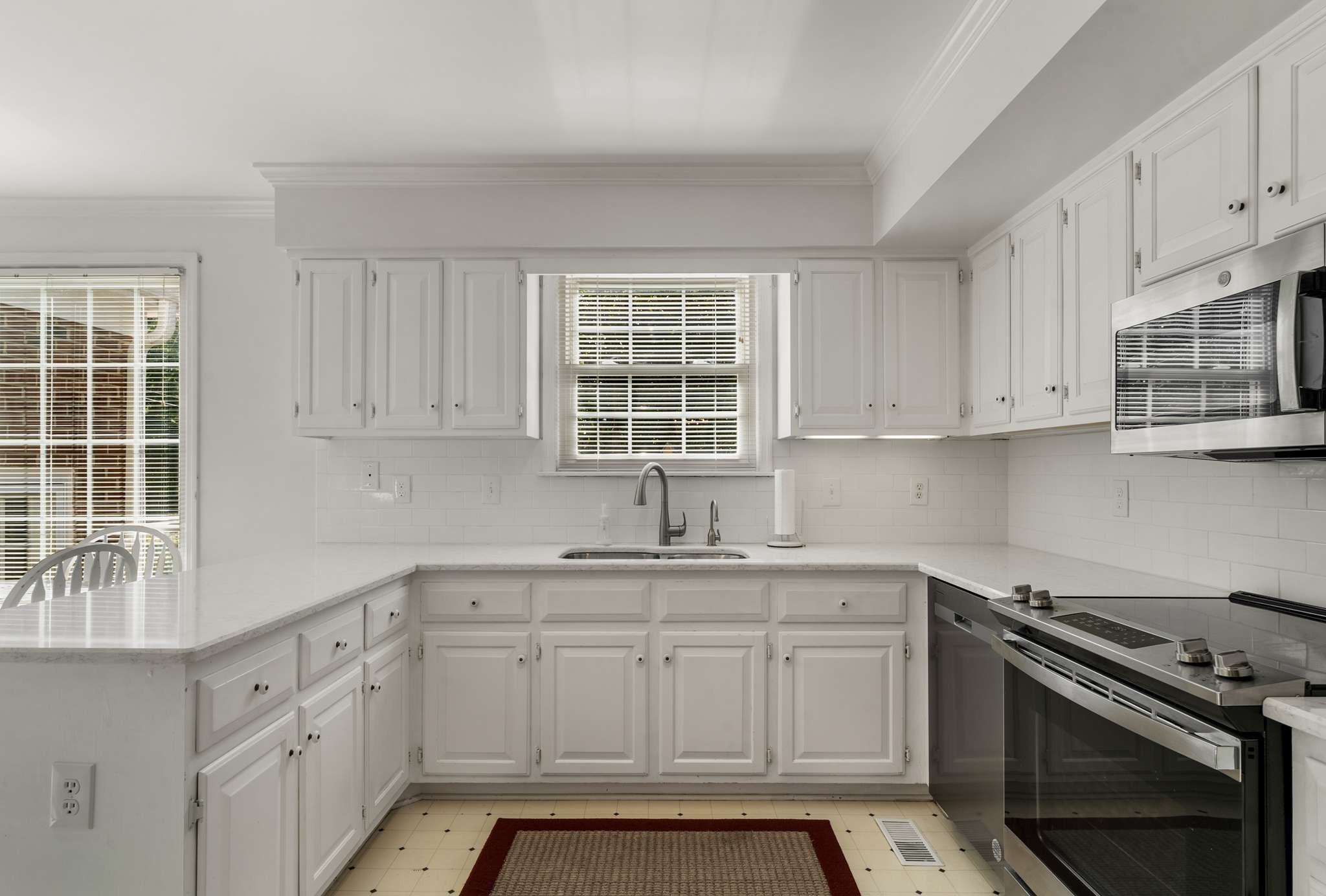 White kitchen with paneled cabinets, stainless steel range, and sink beneath a window.