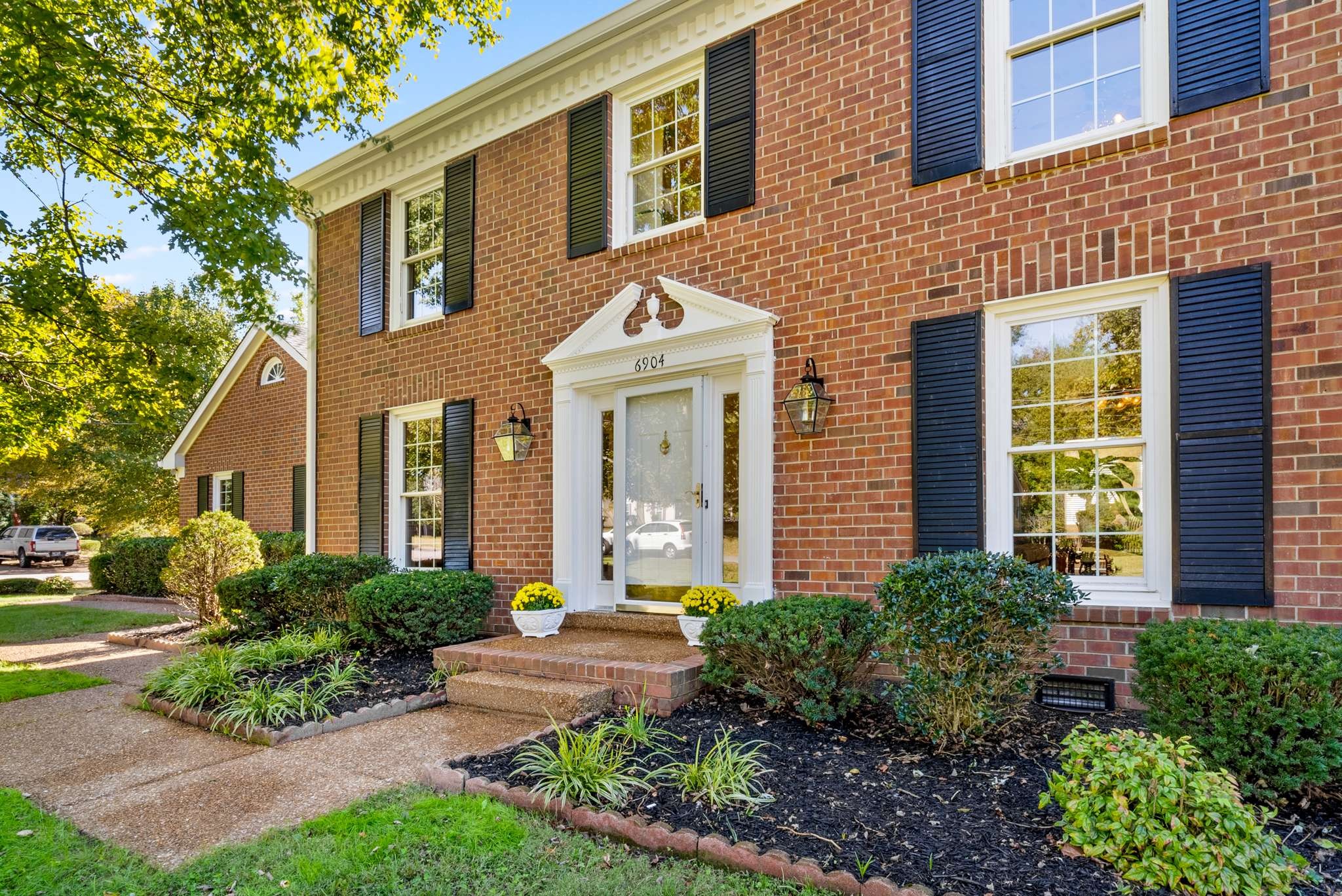 Red-brick home with black shutters, a white entry surround, and landscaped front garden.