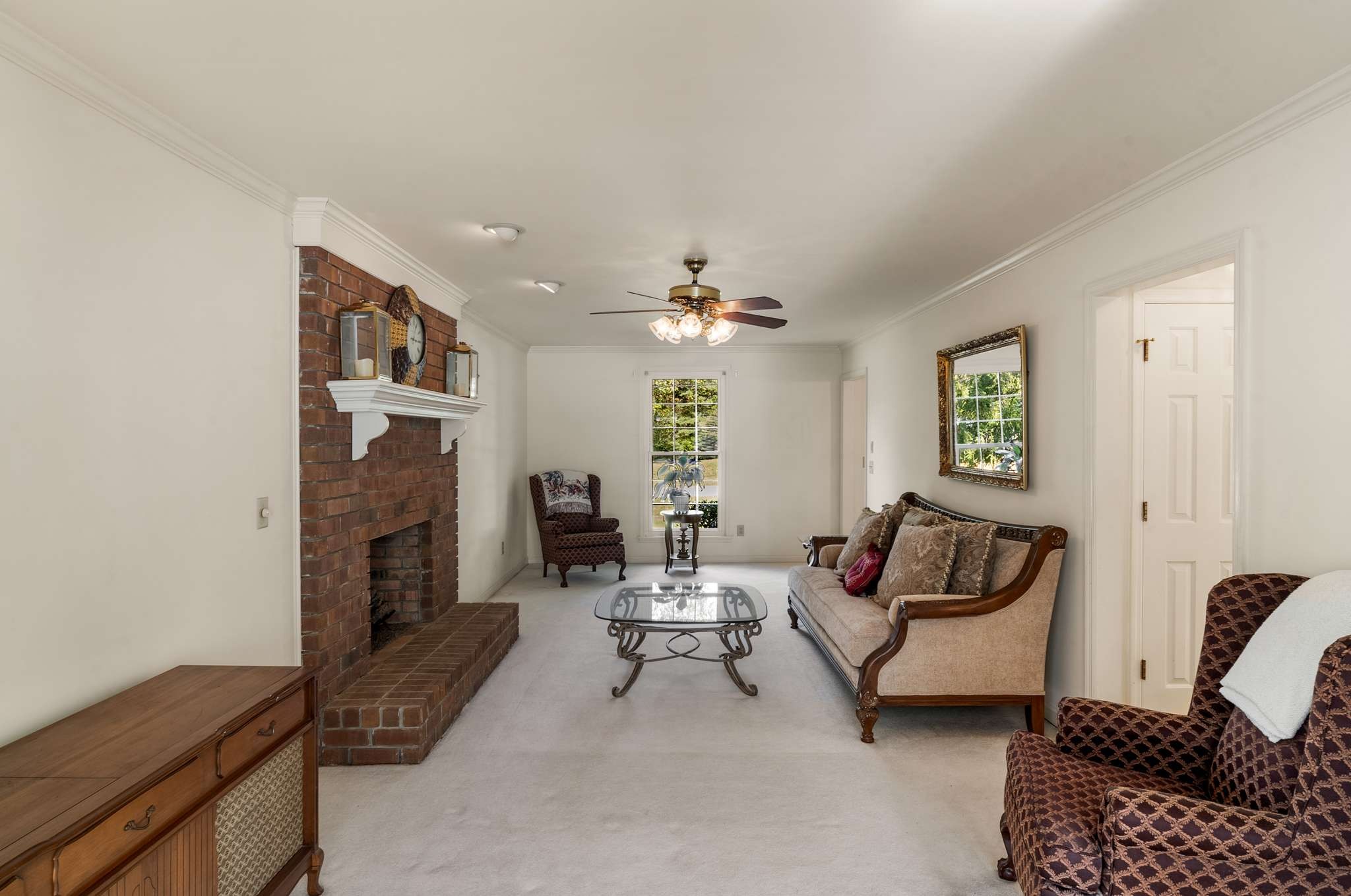 Furnished living room with a brick fireplace, ceiling fan, and traditional seating.