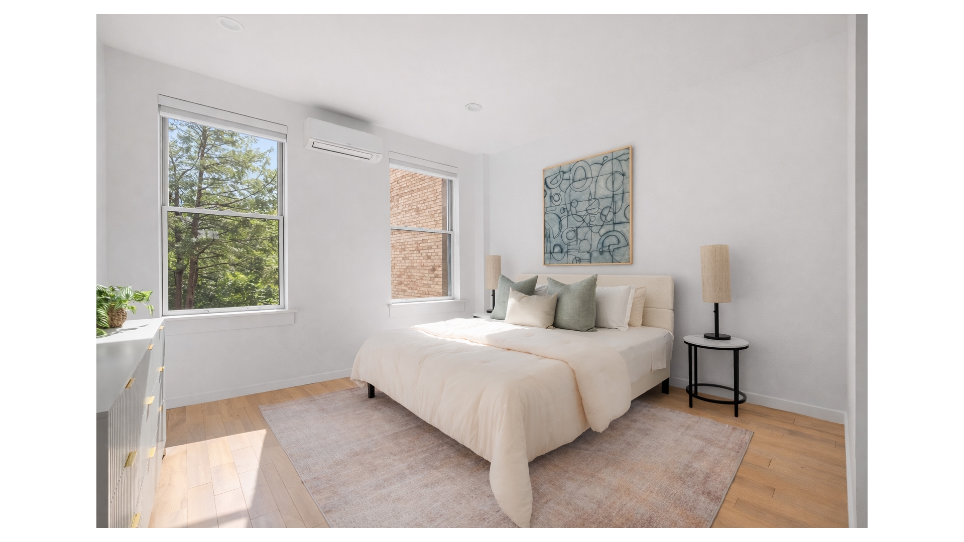 Furnished bedroom with a large bed, abstract art, and windows overlooking trees and a brick wall.