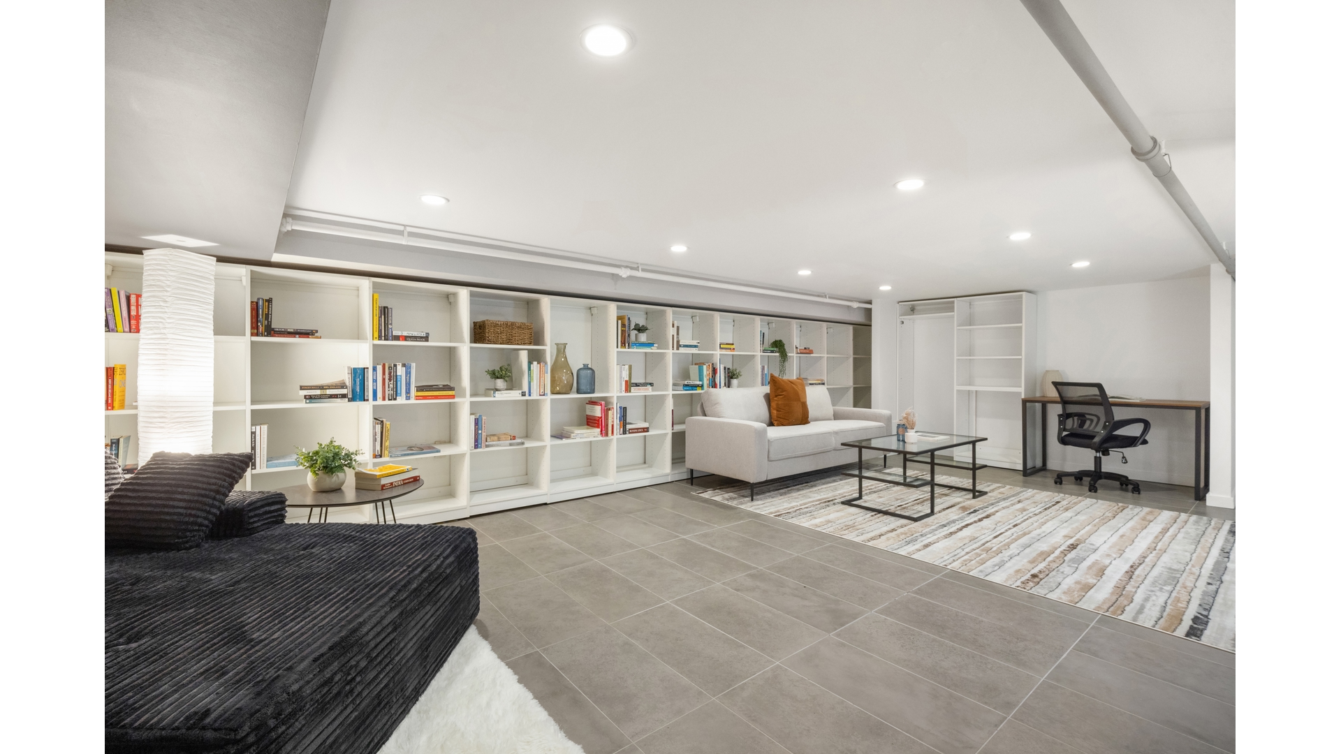 Living area with built-in bookshelves, a sofa, desk, and dark chaise lounge.
