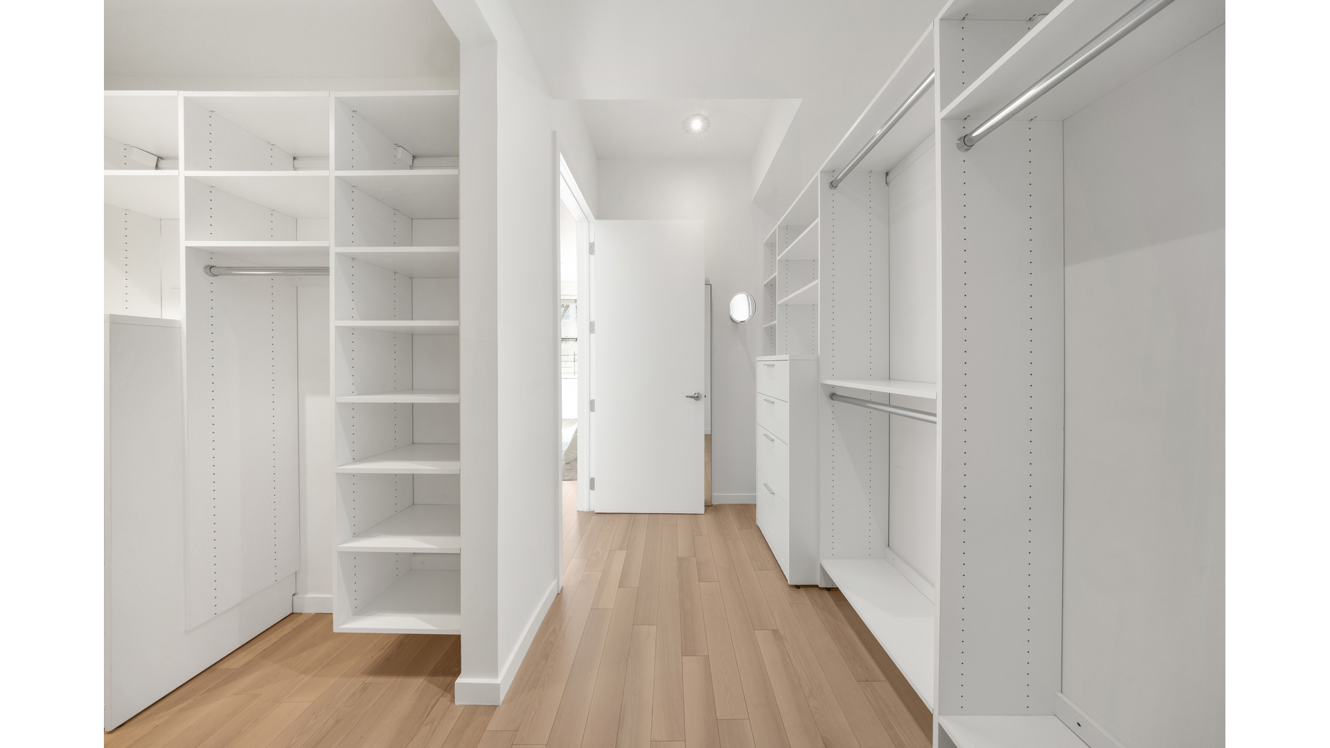Walk-in closet with built-in white shelving, hanging rods, and light wood floors.