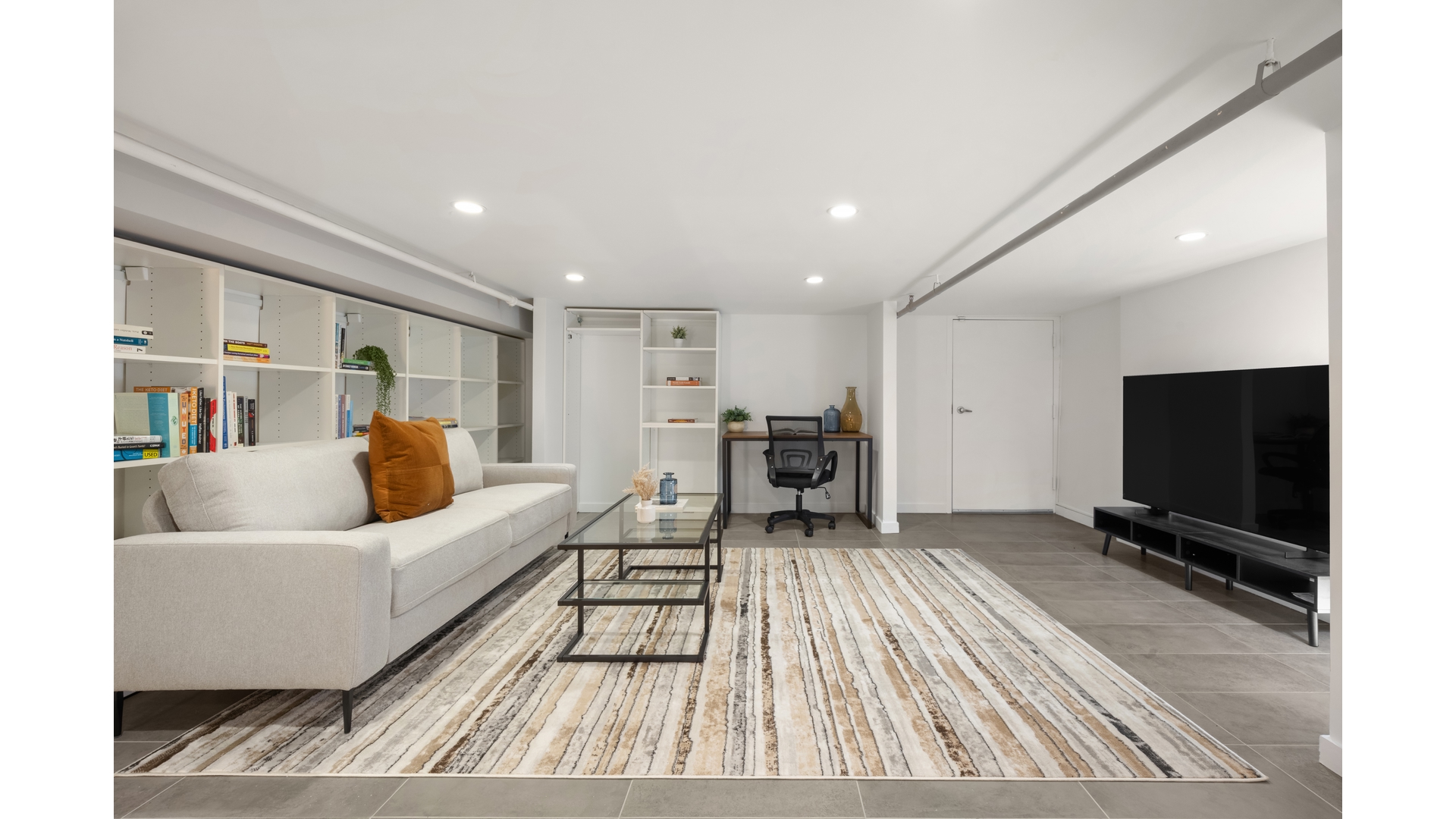 Living room with built-in bookshelves, a light sofa, striped rug, and desk area.