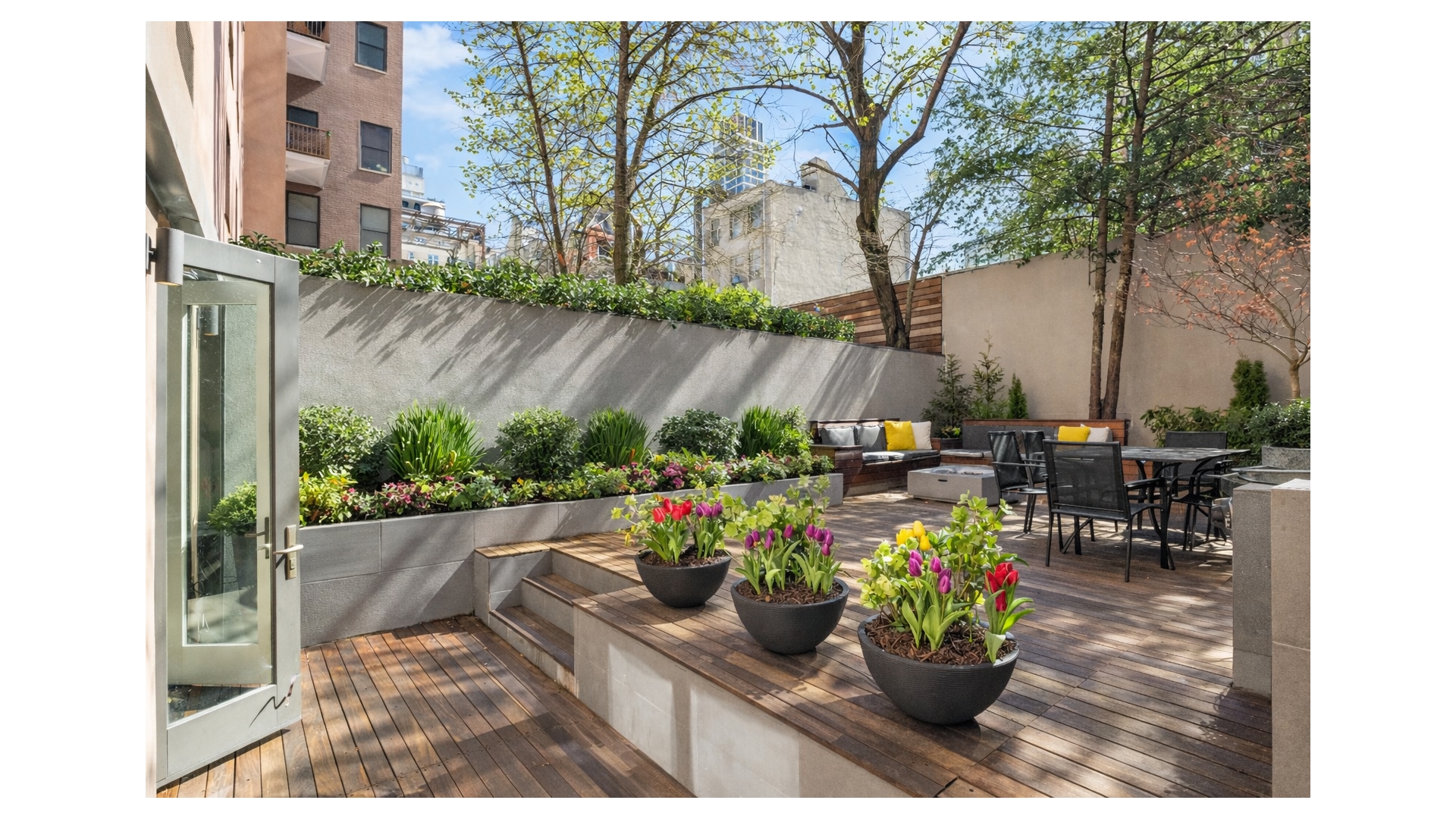 Landscaped terrace with wood decking, colorful tulips, and outdoor lounge and dining furniture.