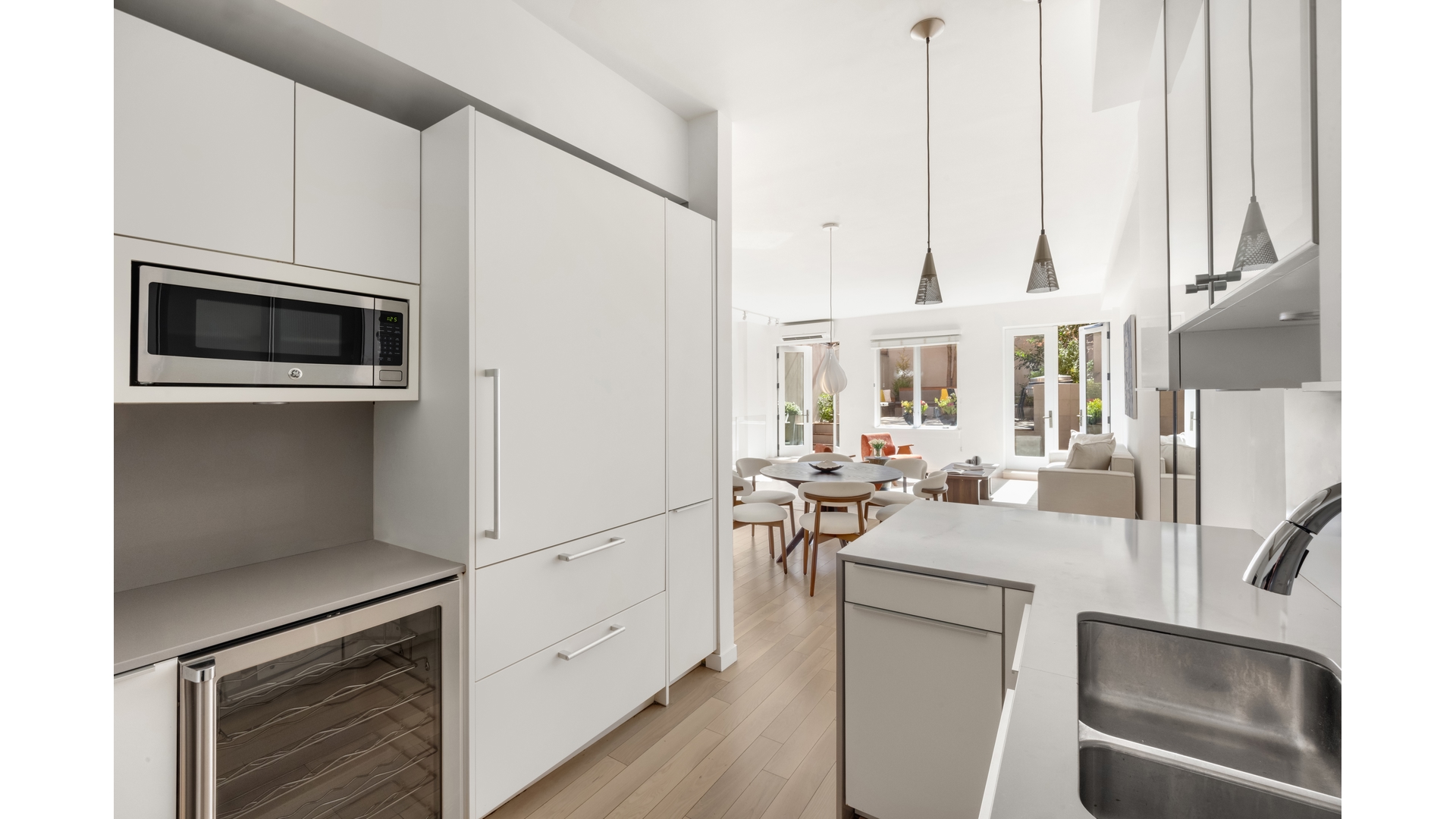 Modern white kitchen with a large island opening onto a dining and living area.