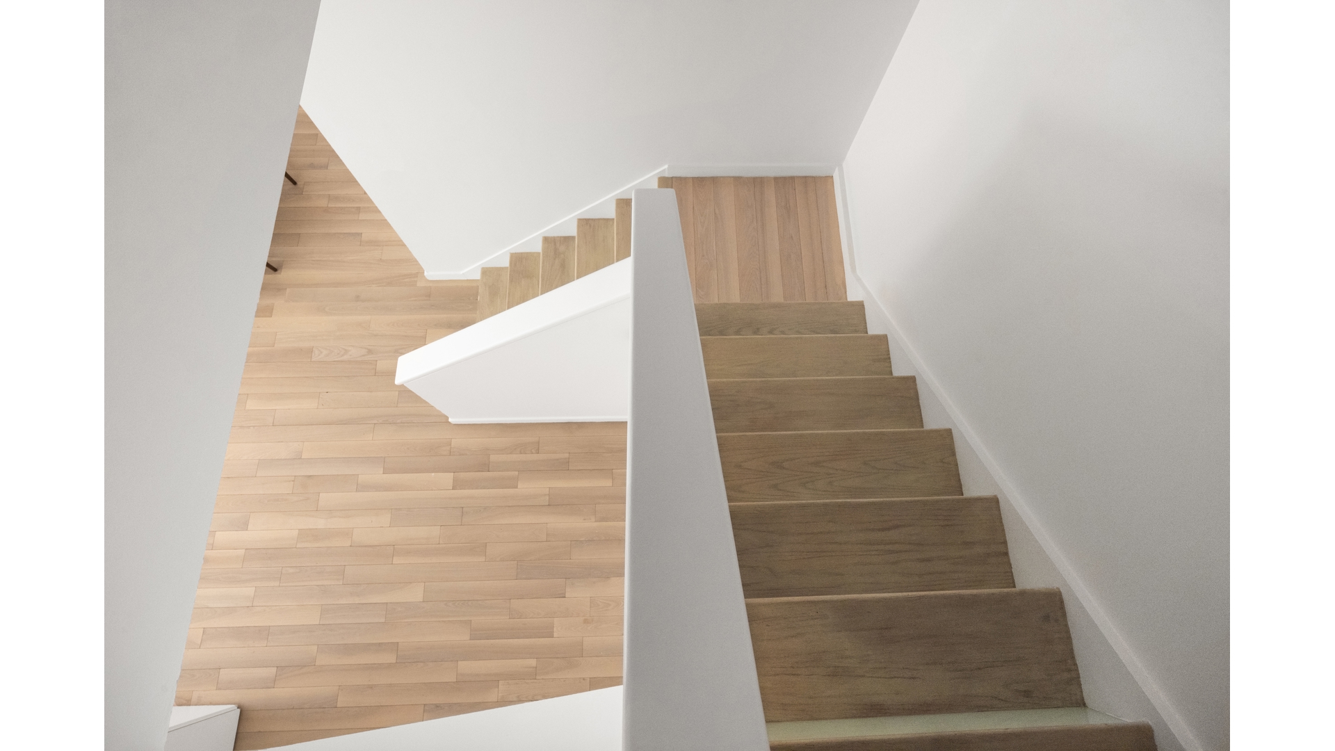 Modern wood staircase with a white partition and light wood-plank flooring.