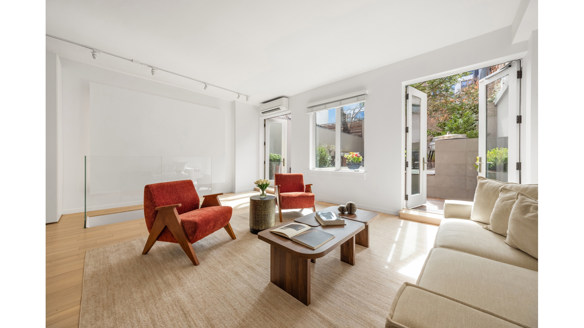 Bright living room with rust-red armchairs and open doors to a leafy terrace.