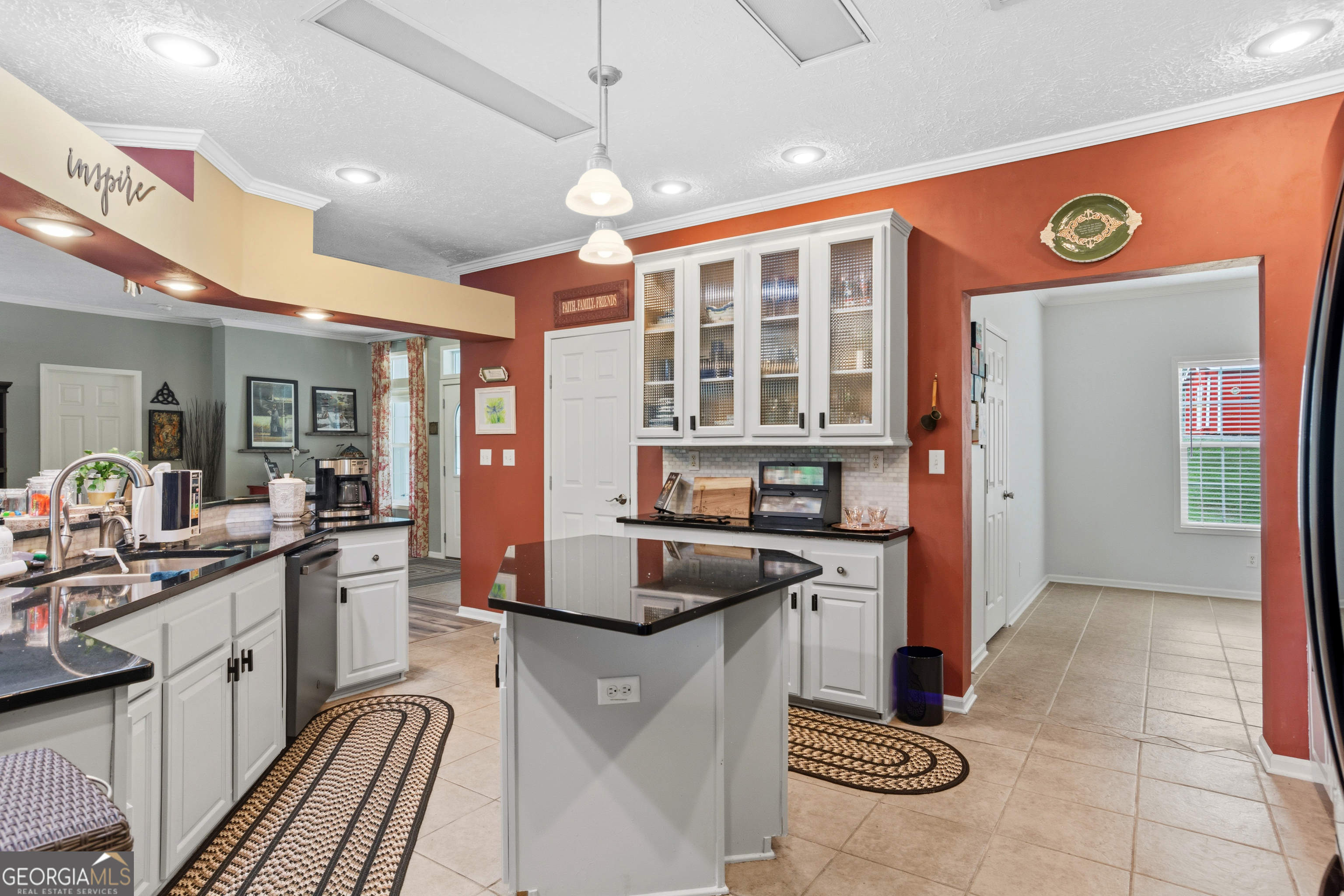 Kitchen with a black-topped island, white glass-front cabinets, and a red accent wall.