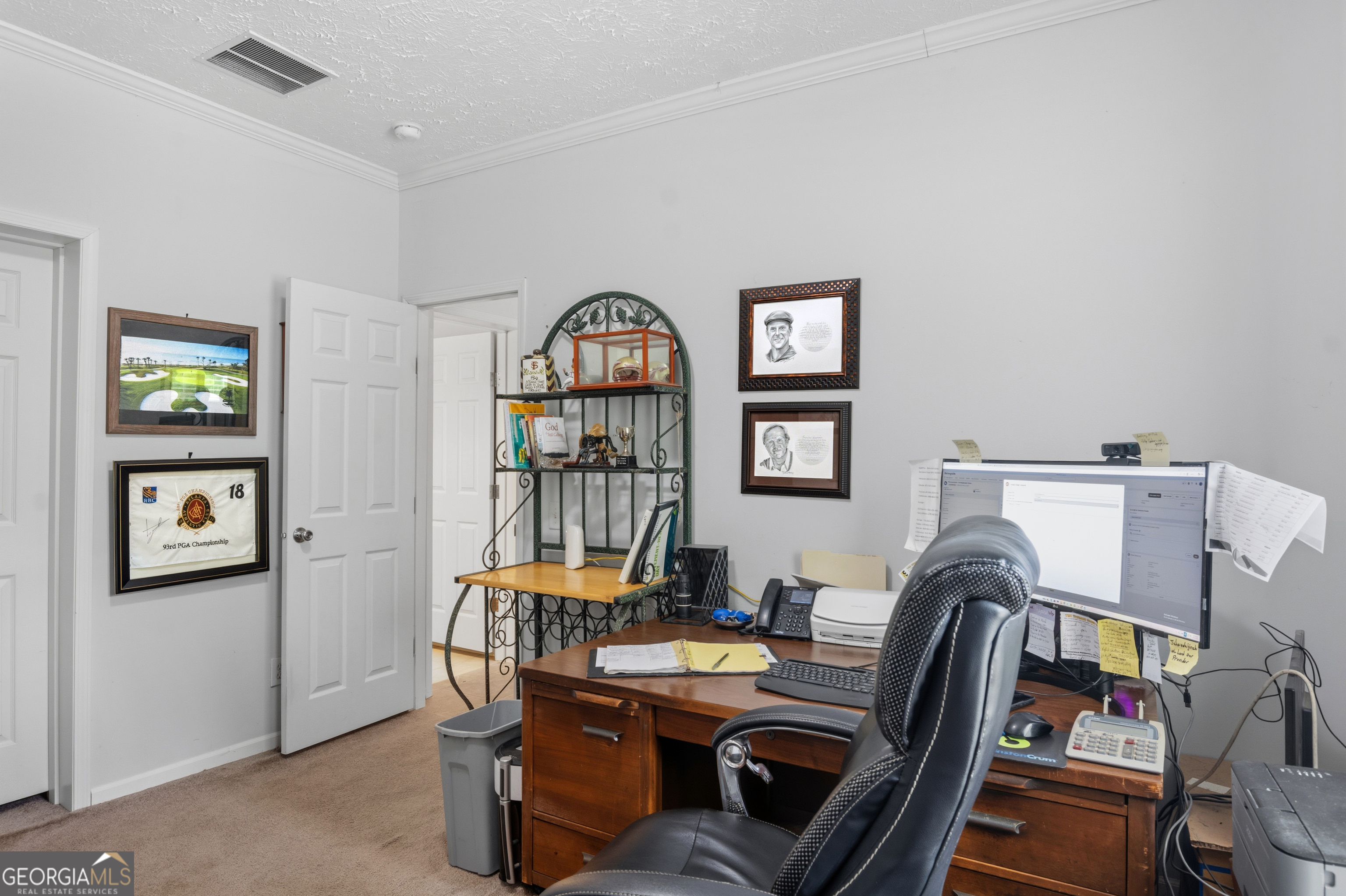 Home office with a wooden desk, black chair, computer, and framed golf memorabilia.