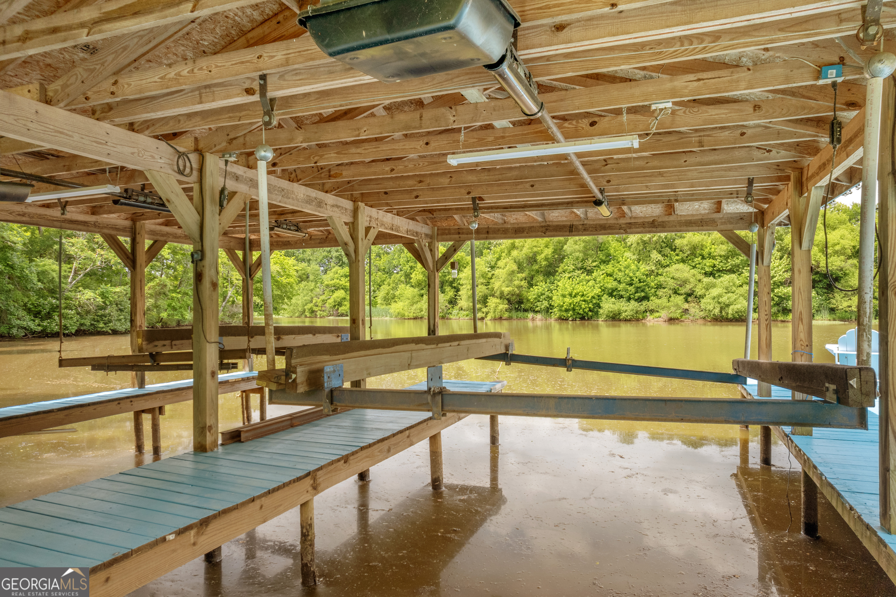Covered wooden boat dock with blue walkways and boat lifts over a tree-lined lake.