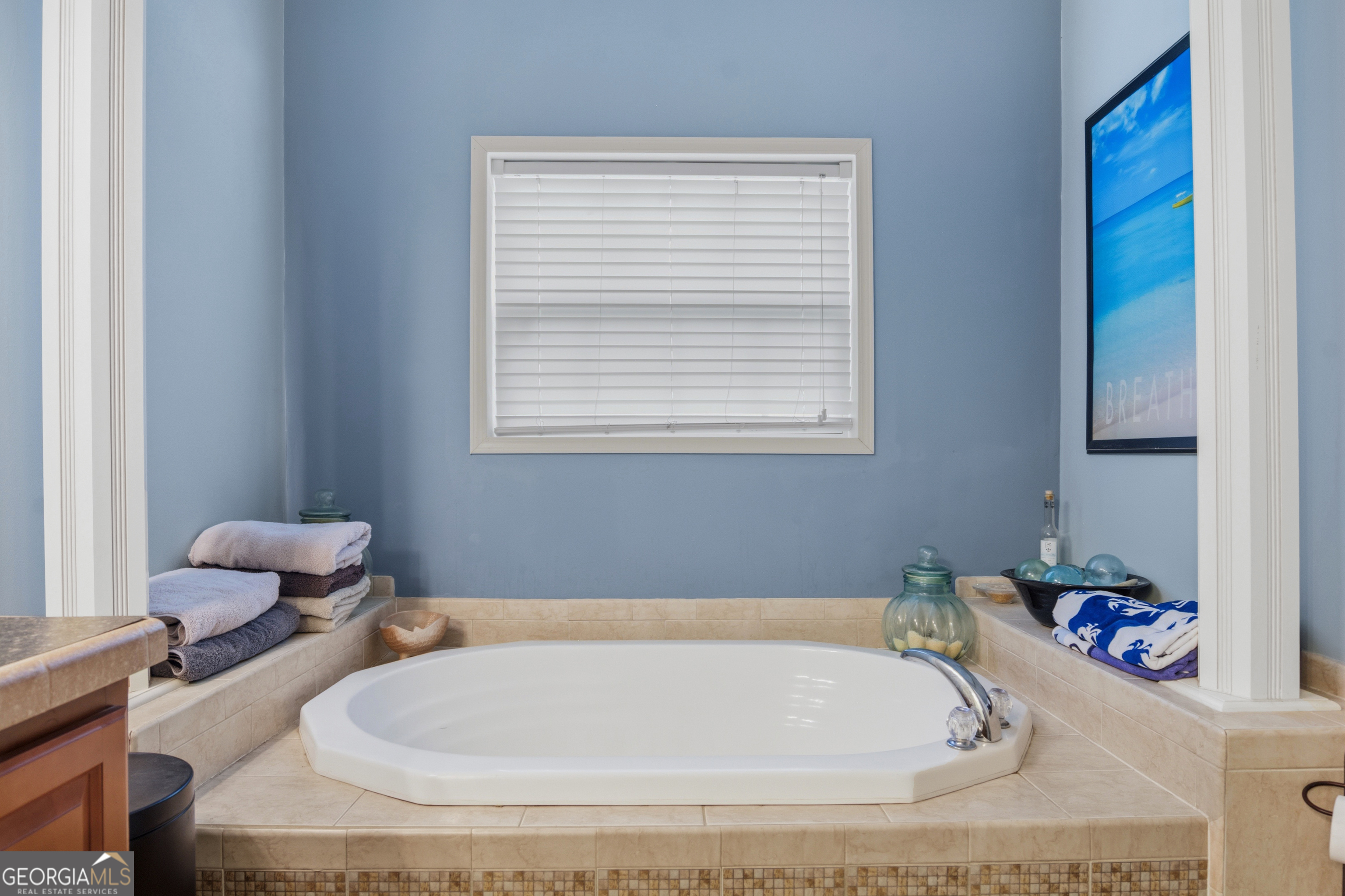 Bathroom with a large corner soaking tub, beige tile surround, folded towels, and blue walls.
