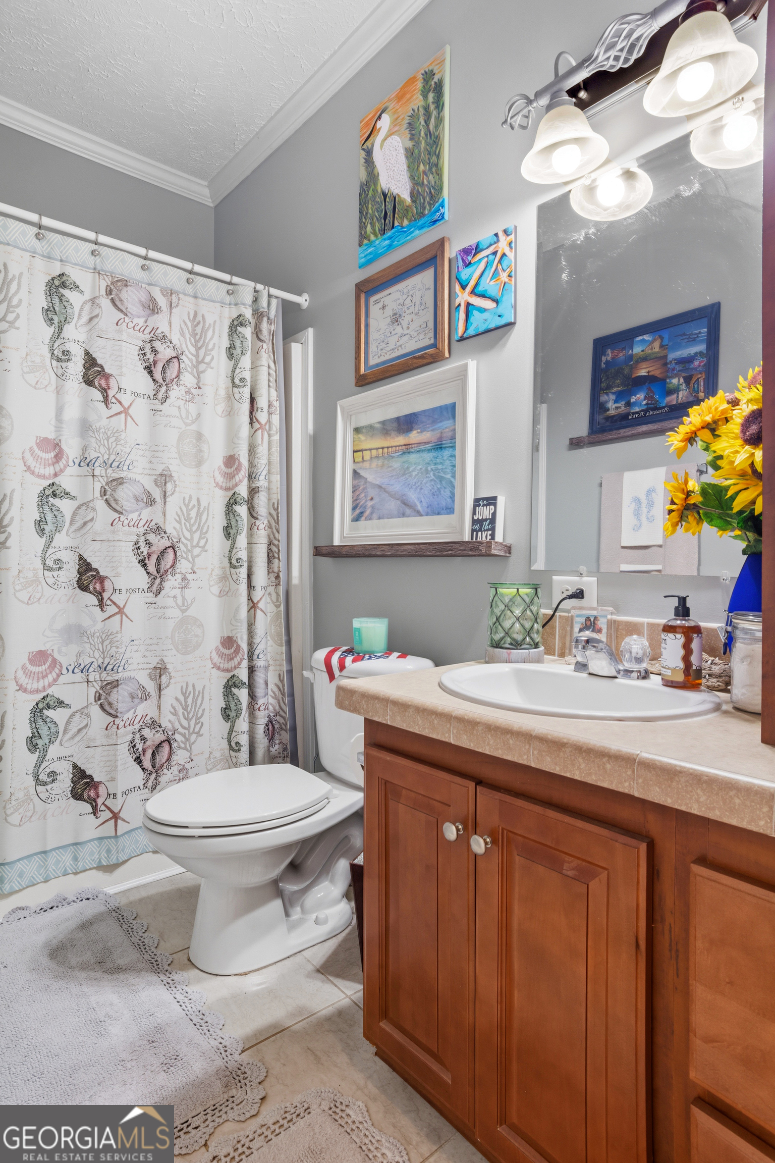 Bathroom with a wood vanity, shell-patterned shower curtain, and lake-themed wall art.
