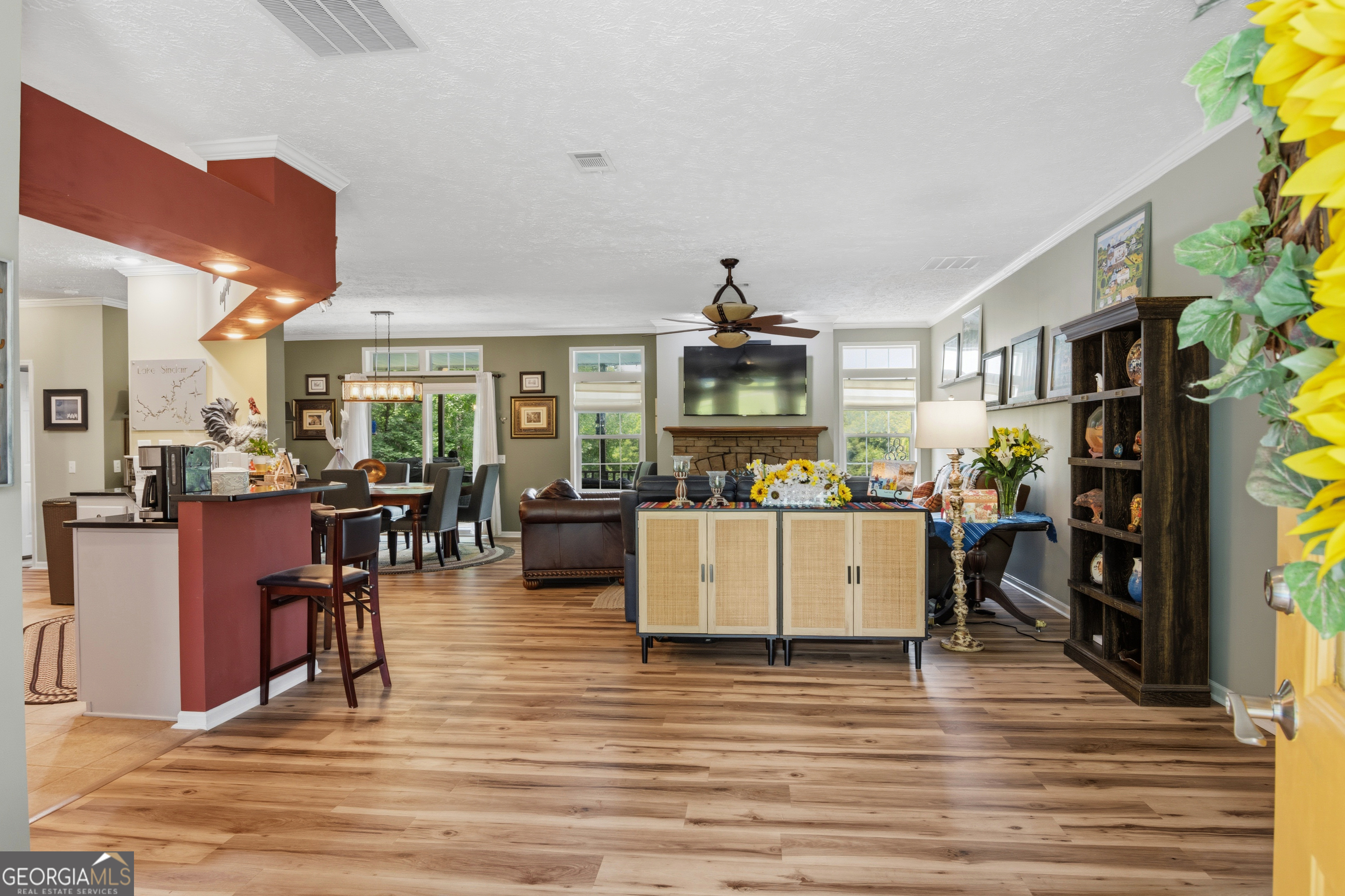 Open-plan living room with a stone fireplace, dining area, and kitchen with a red breakfast bar.