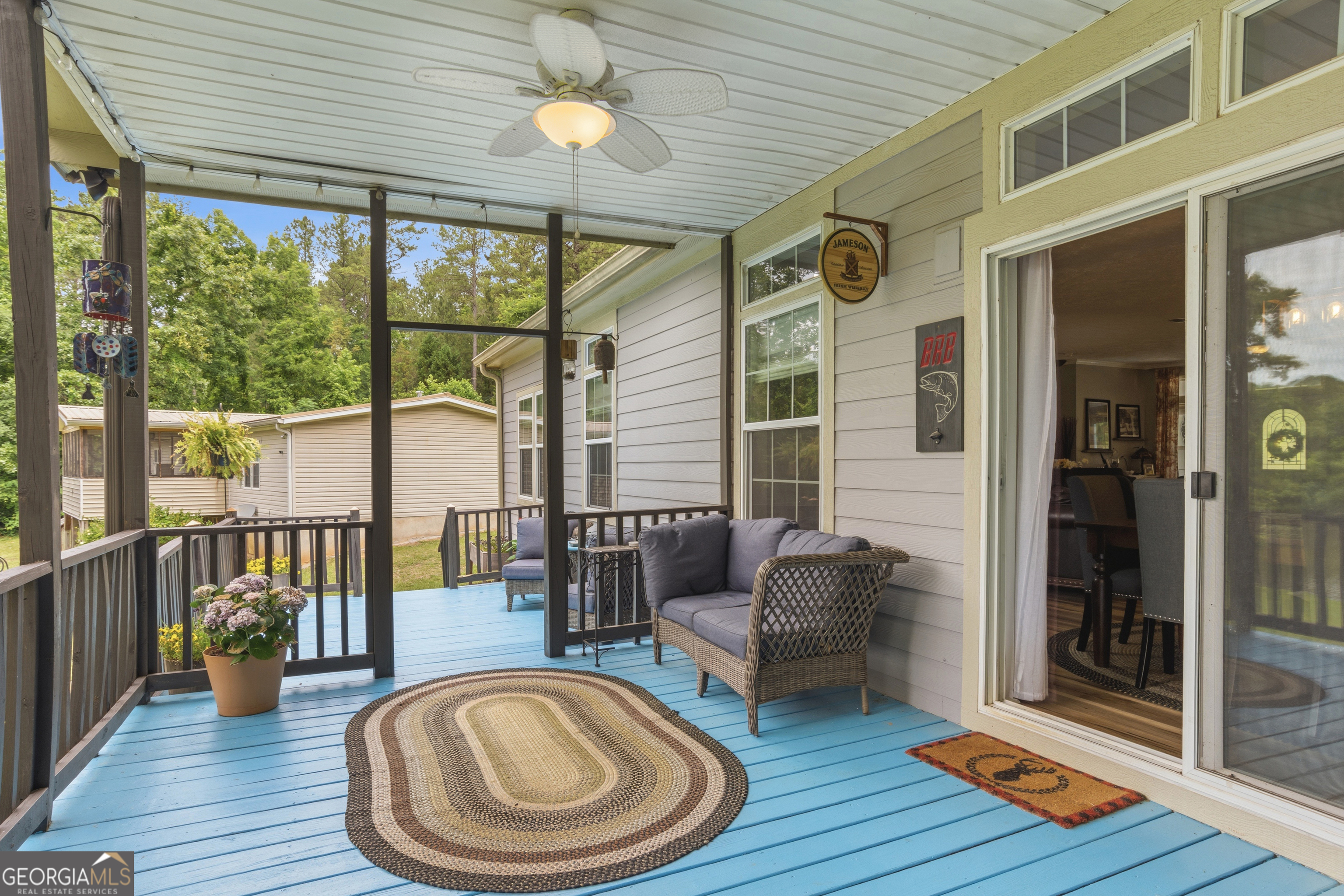Covered porch with blue decking, wicker seating, a ceiling fan, and potted flowers.