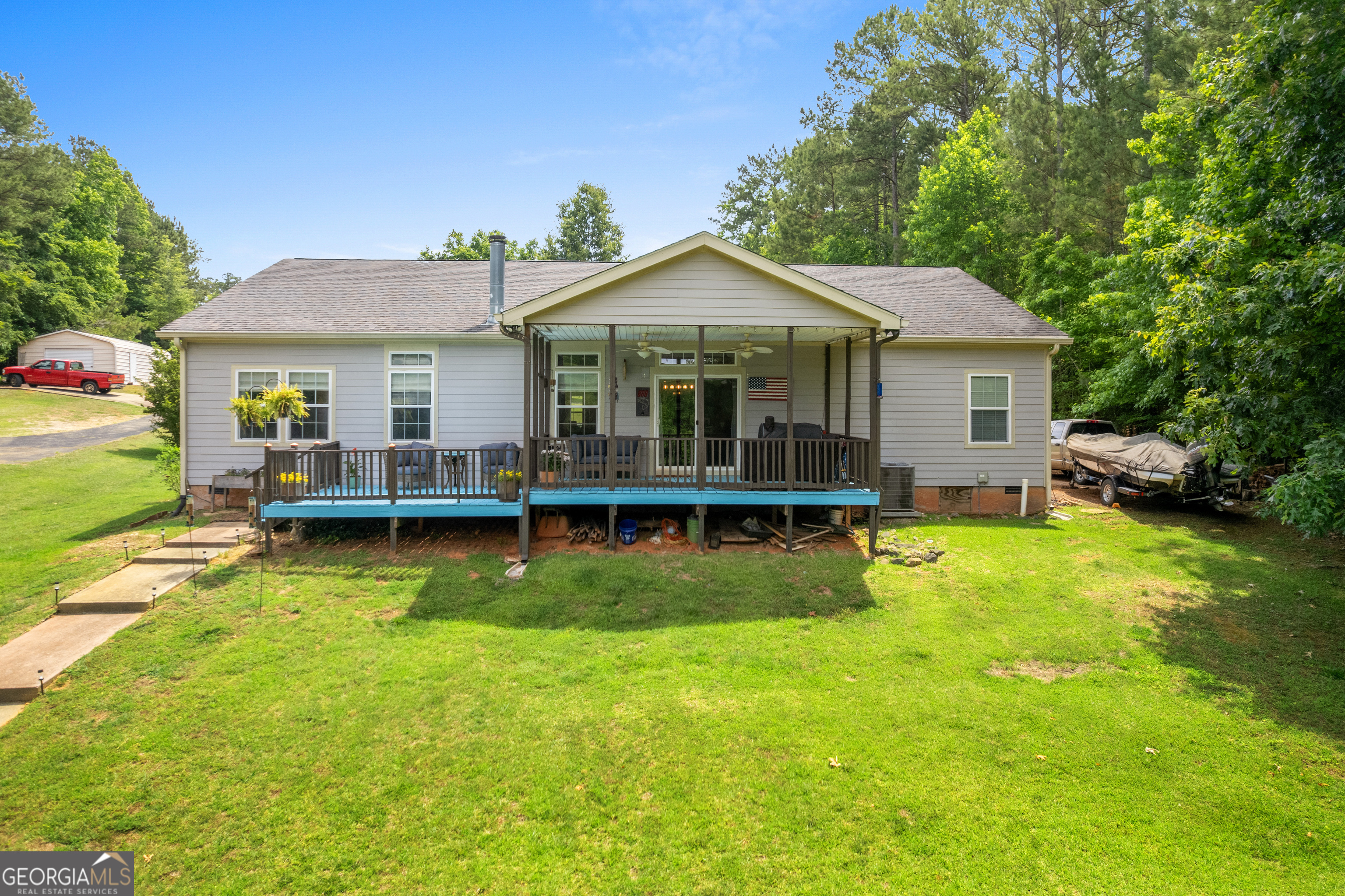 Rear of a gray house with a covered raised deck, broad lawn, and mature trees.