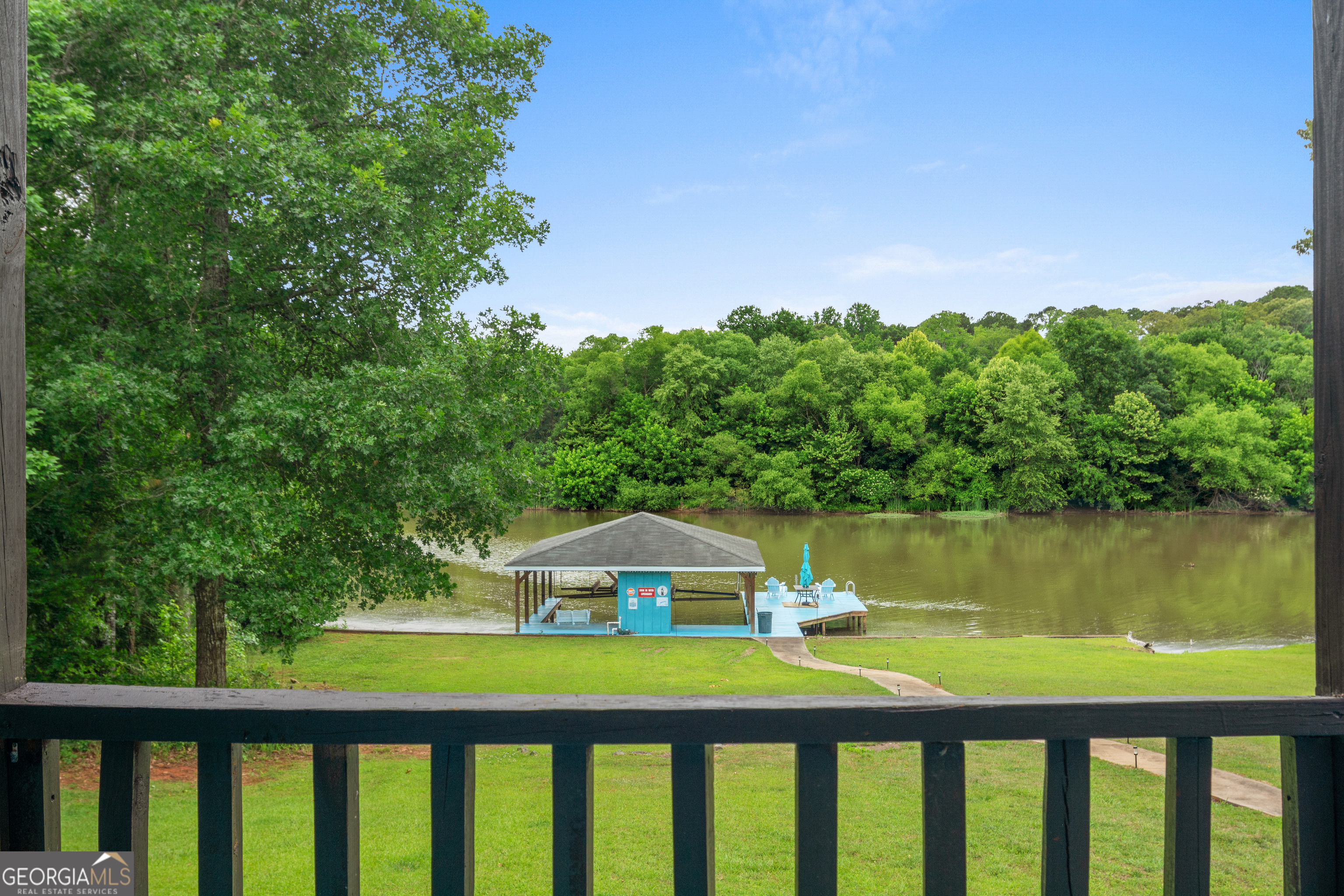 Lake and covered dock seen from a grassy waterfront property, framed by a deck railing.